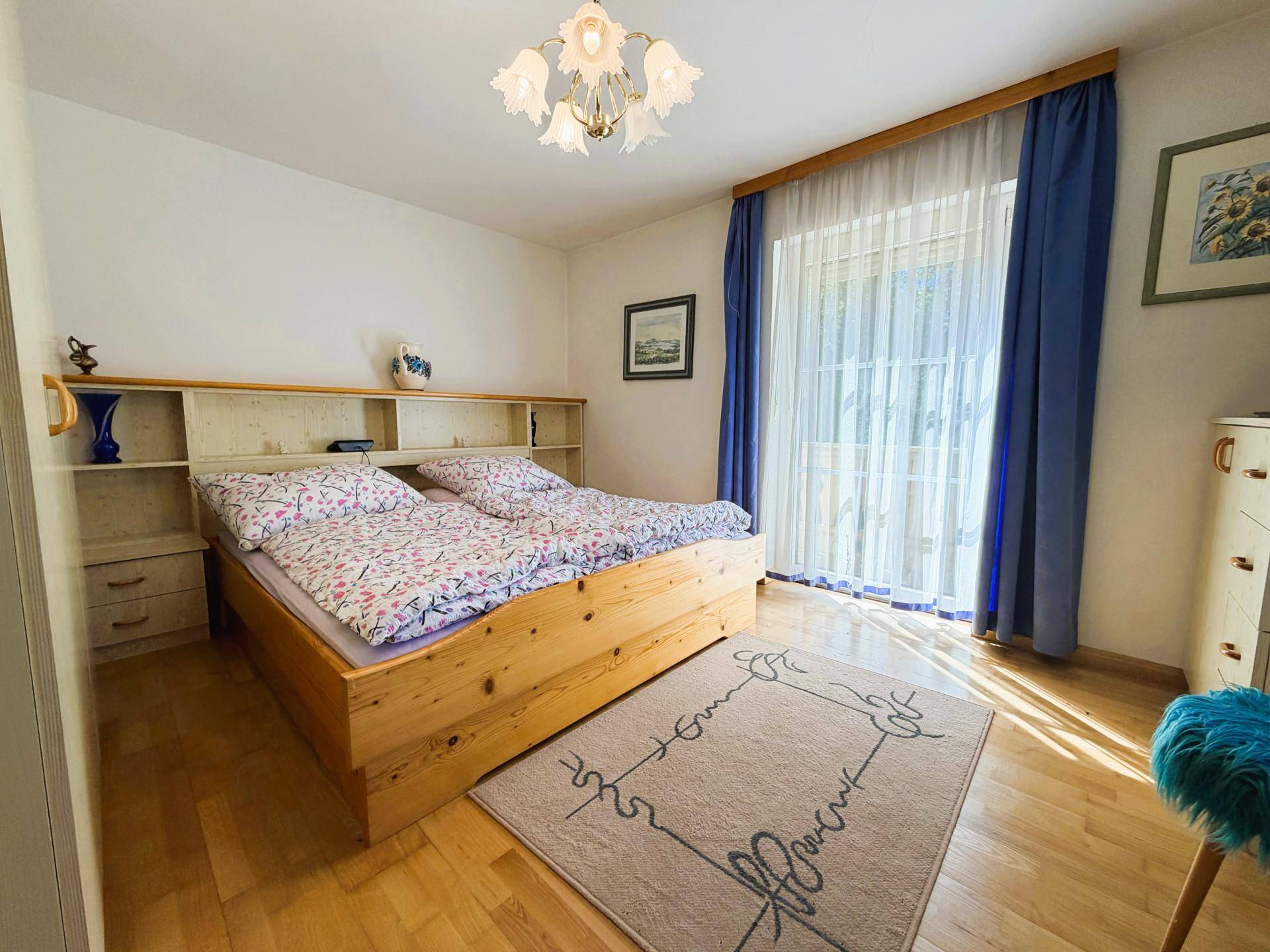 Schlafzimmer mit Holzbett, Parkettboden und Zugang zu einem Balkon.