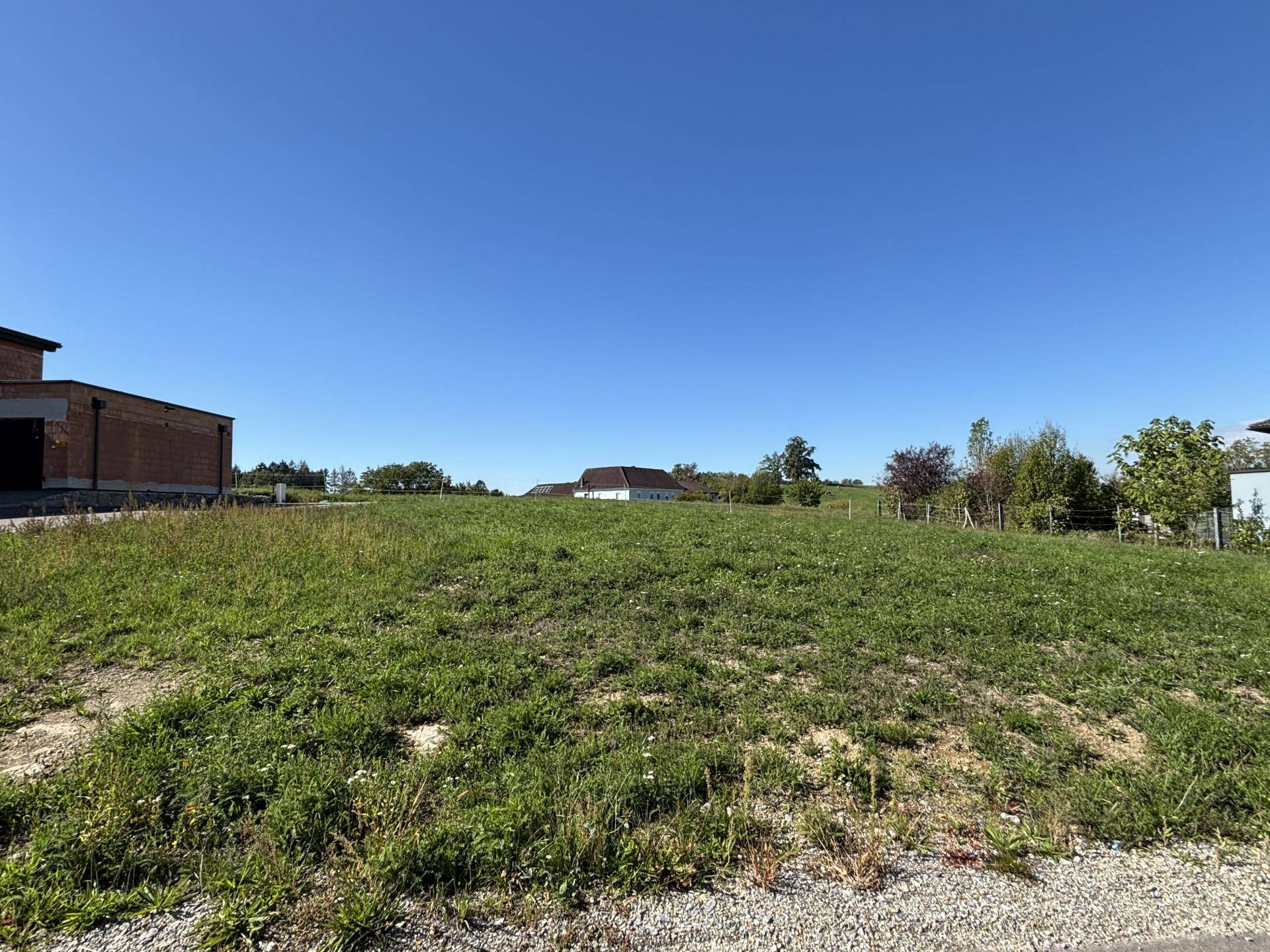 Sonniges, offenes Grundstück mit weitem Blick auf die umliegende grüne Landschaft und vereinzelte Häuser.