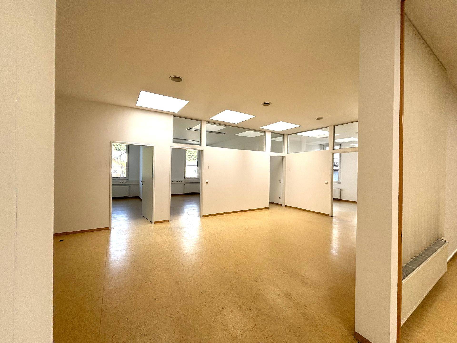Heller Bürobereich mit mehreren Zugängen zu Einzelbüros und großen Fenstern, die viel Tageslicht hereinlassen.