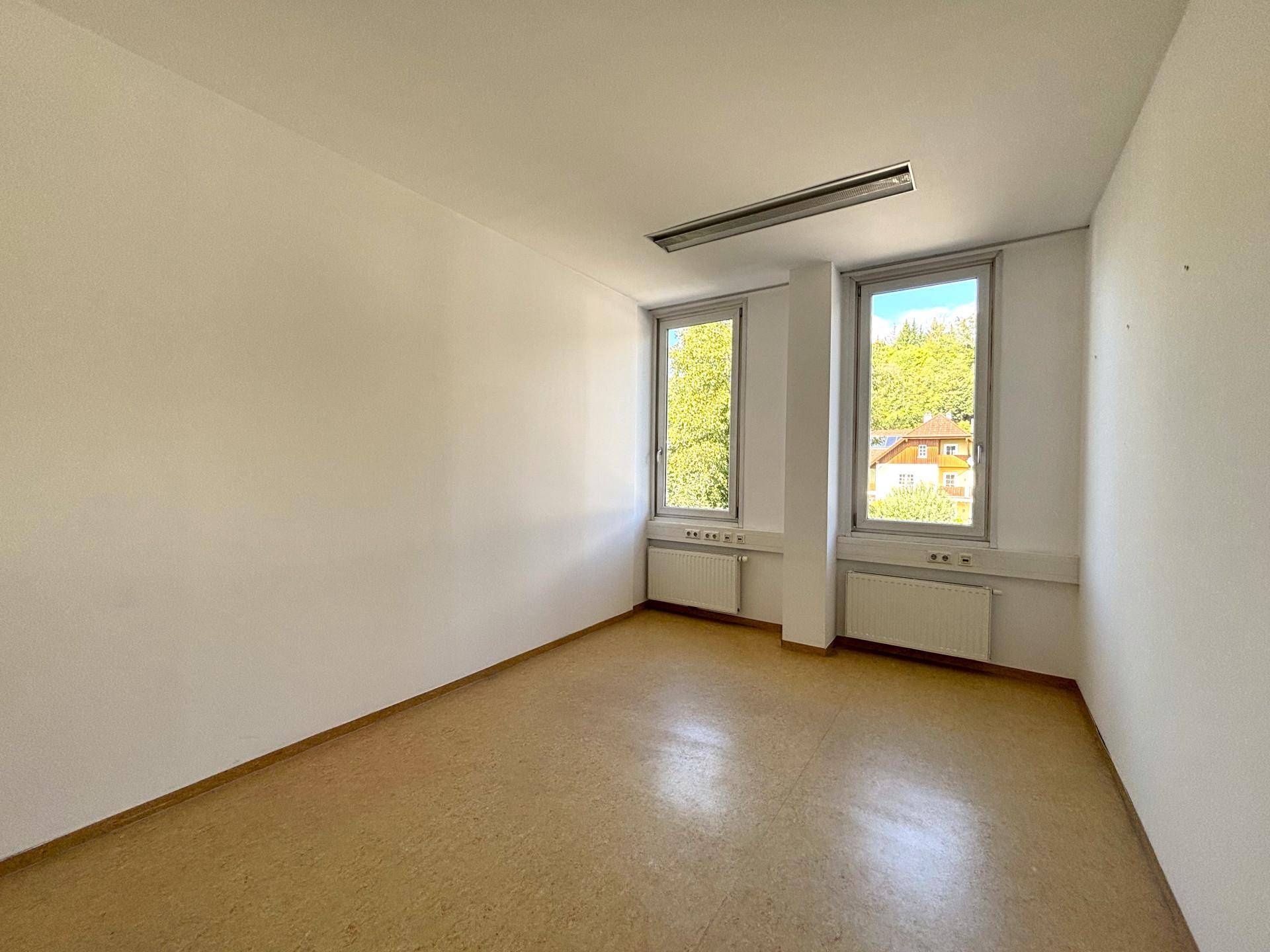 Einzelbüro mit zwei hohen Fenstern, die viel Tageslicht hereinlassen, und einem strapazierfähigen Linoleumboden.