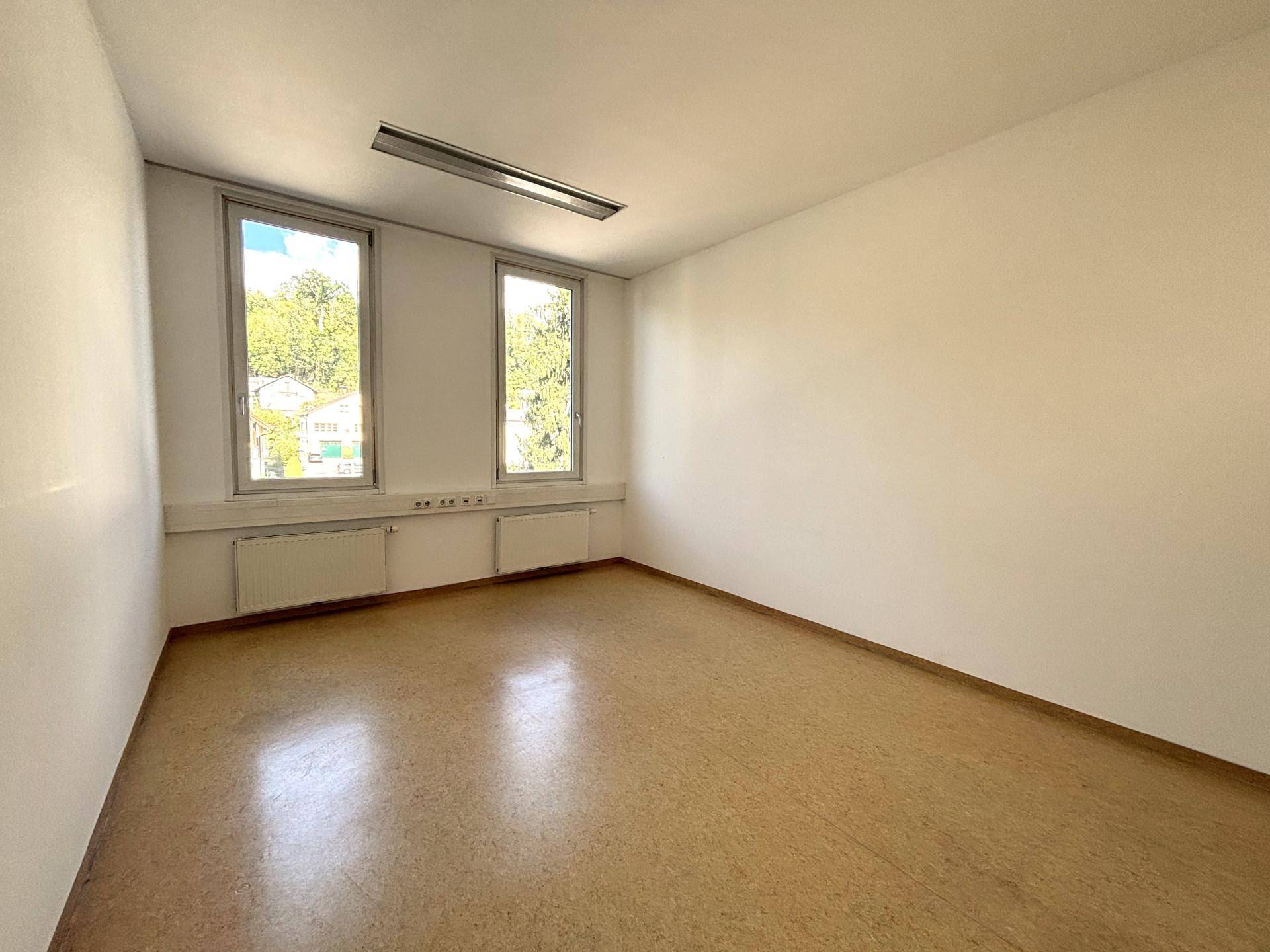 Helles Einzelbüro mit zwei Fenstern, die einen Blick ins Grüne ermöglichen, und einem robusten Linoleumboden.