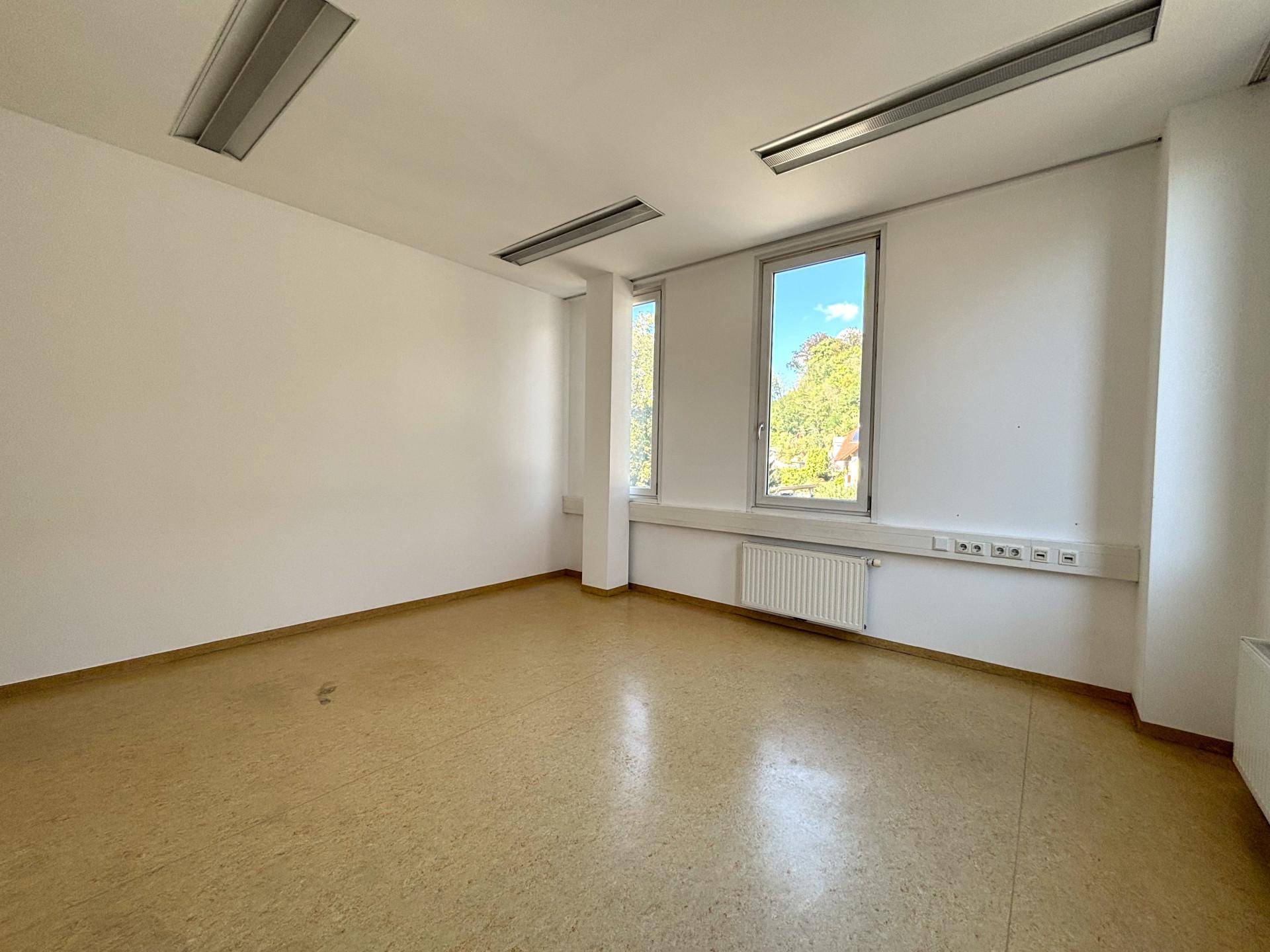 Helles Büro mit drei Fenstern, die einen Blick ins Grüne ermöglichen, und einem strapazierfähigen Linoleumboden.