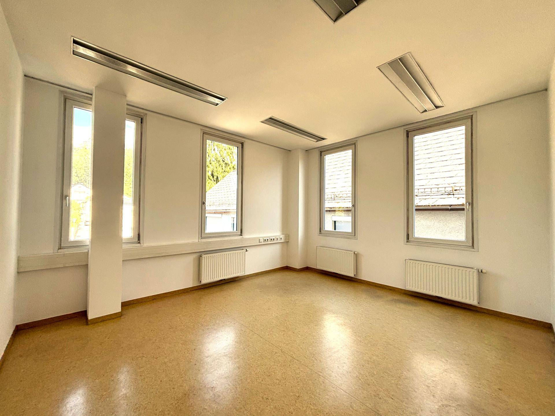 Geräumiges Büro mit vier hohen Fenstern, die viel Tageslicht bieten, und einem praktischen Linoleumboden.