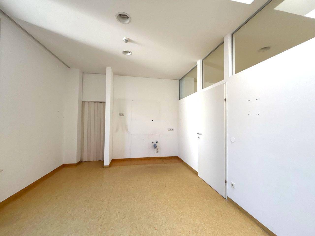Raum mit Linoleumboden, weißen Wänden und einer Trennwand, die einen Bereich mit Anschlüssen abgrenzt.
