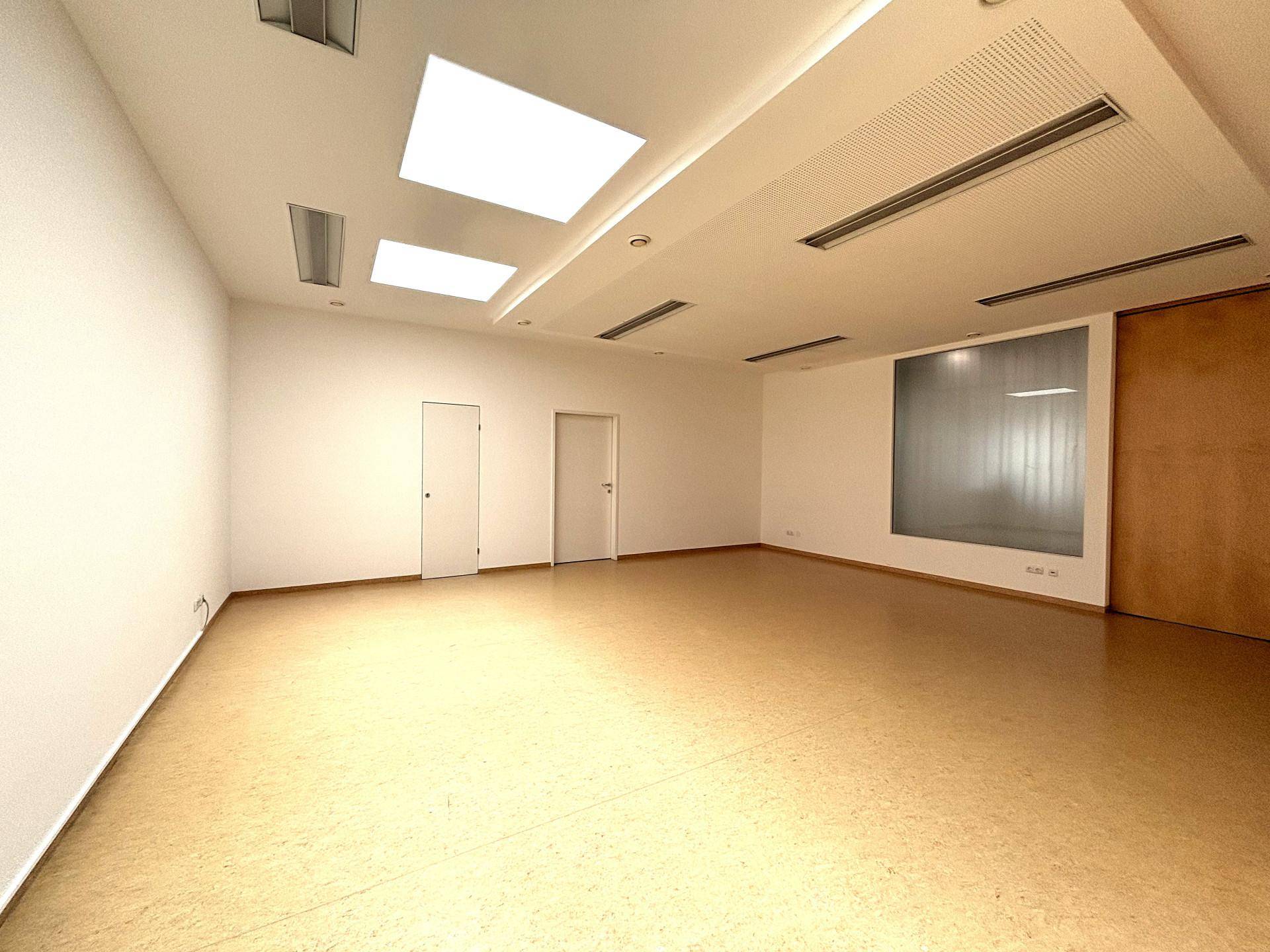 Großer, heller Büroraum mit Linoleumboden, abgehängter Decke und integrierter Beleuchtung.