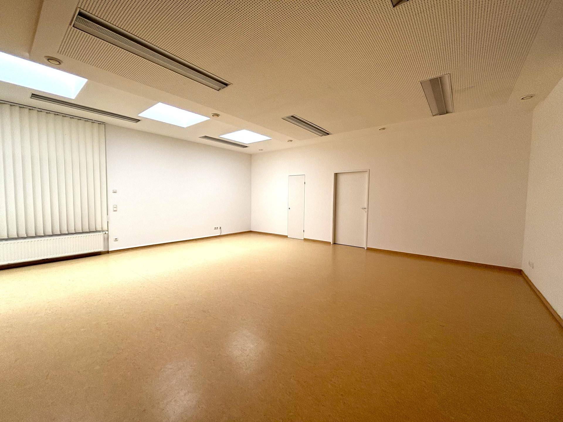 Geräumiger Büroraum mit Linoleumboden, weißen Wänden und einer abgehängten Decke mit integrierter Beleuchtung.