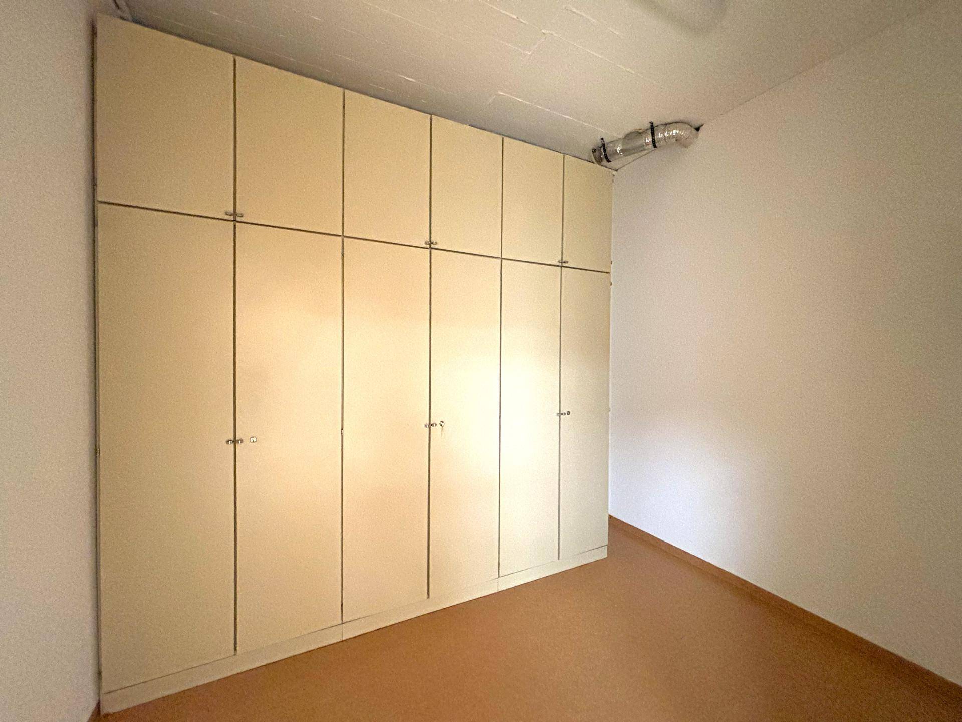 Kleiner Raum mit Einbauschränken entlang einer Wand und einem strapazierfähigen Linoleumboden.