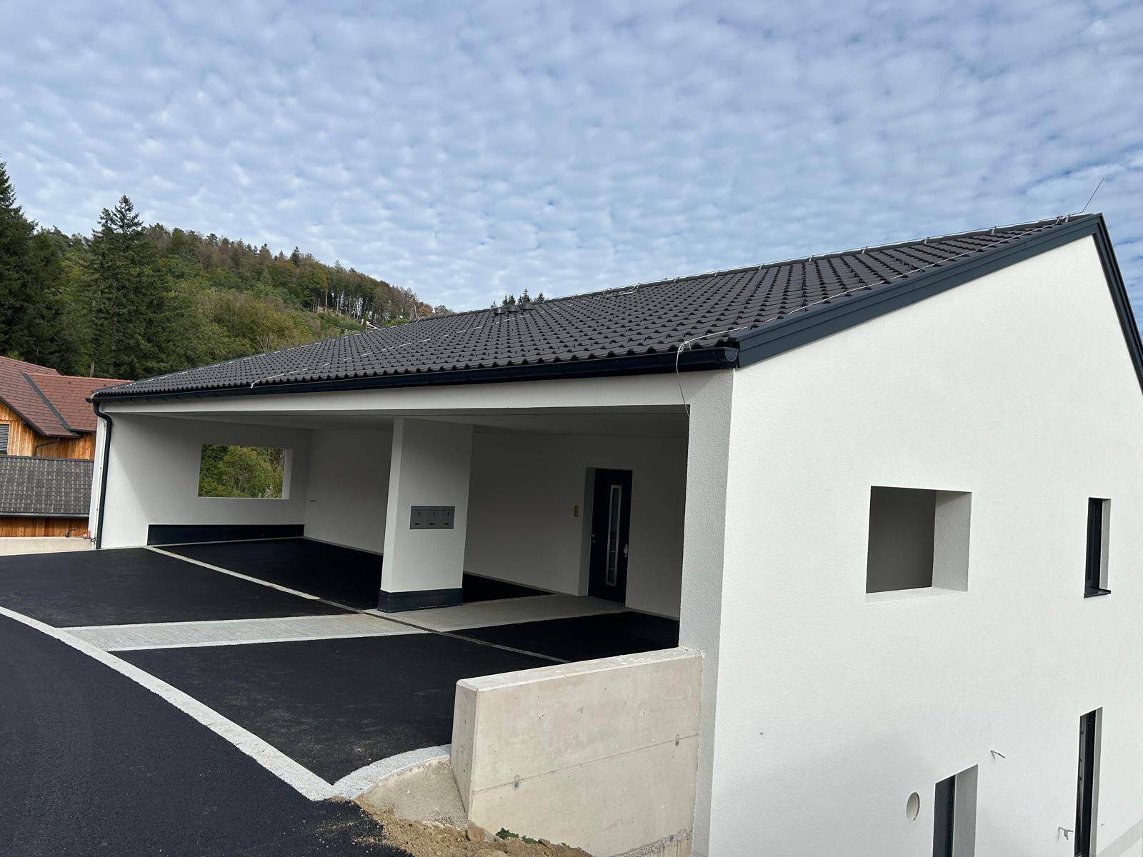 Modernes Gebäude mit weißer Fassade und integriertem Carport für mehrere Fahrzeuge.