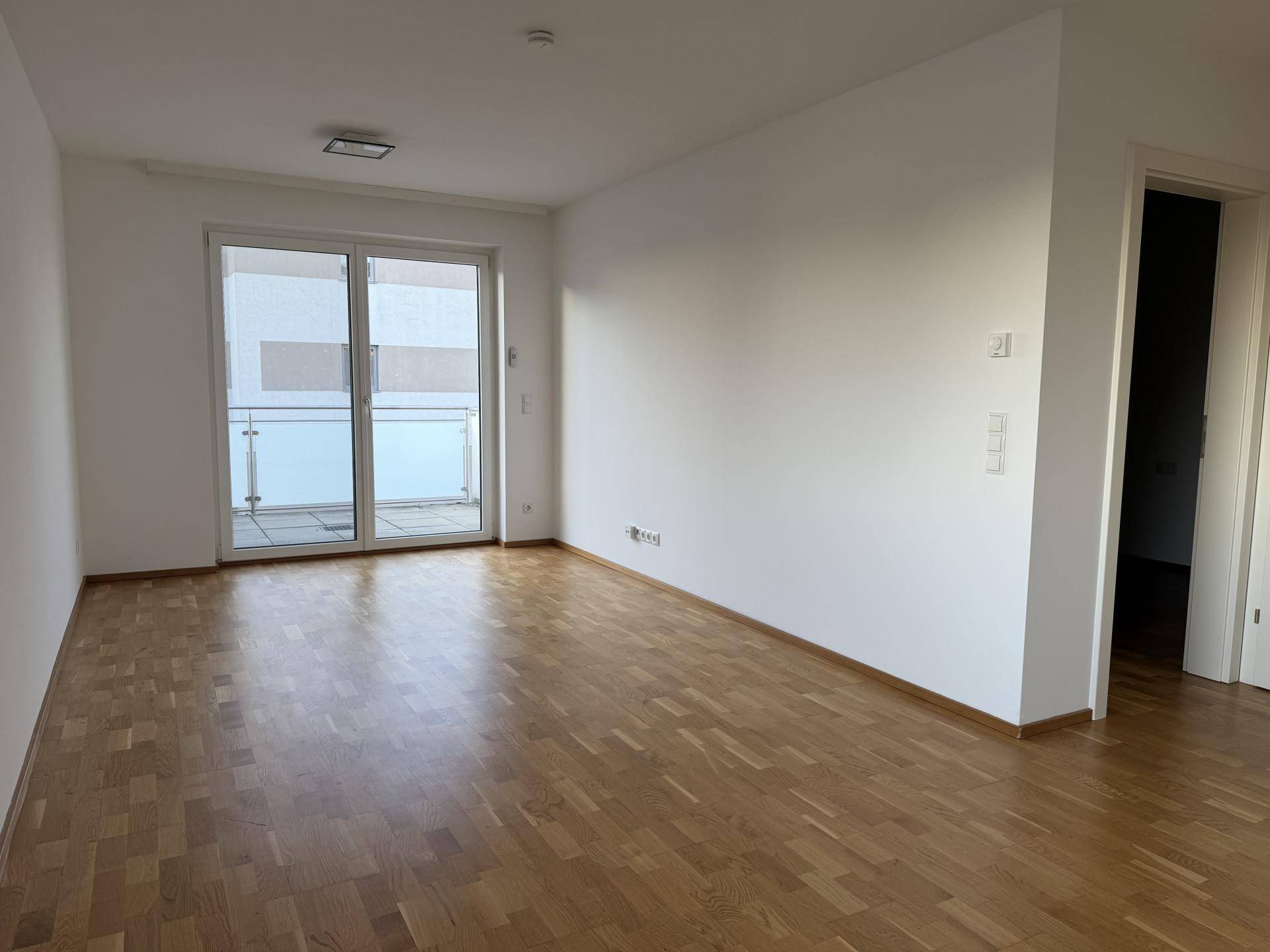 Heller, leerer Raum mit Parkettboden und Zugang zu einem Balkon, ideal für ein Wohnzimmer.
