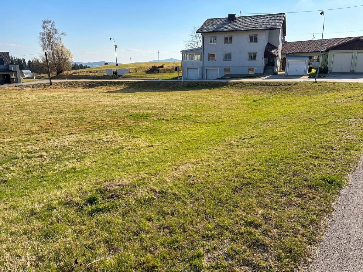 Grüne Wiese im Vordergrund mit einem Mehrfamilienhaus und Garagen im ländlichen Umfeld.