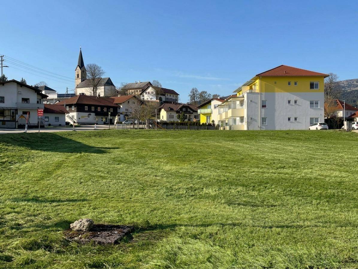 Grüne Wiese mit Blick auf ein Dorf, eine Kirche und ein modernes Apartmentgebäude.