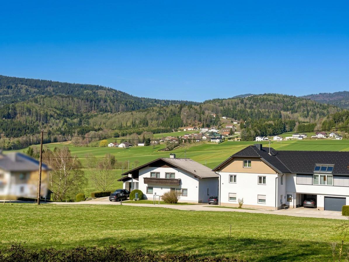 Nahaufnahme von zwei Wohnhäusern in einer idyllischen Landschaft mit grünen Wiesen und bewaldeten Bergen.
