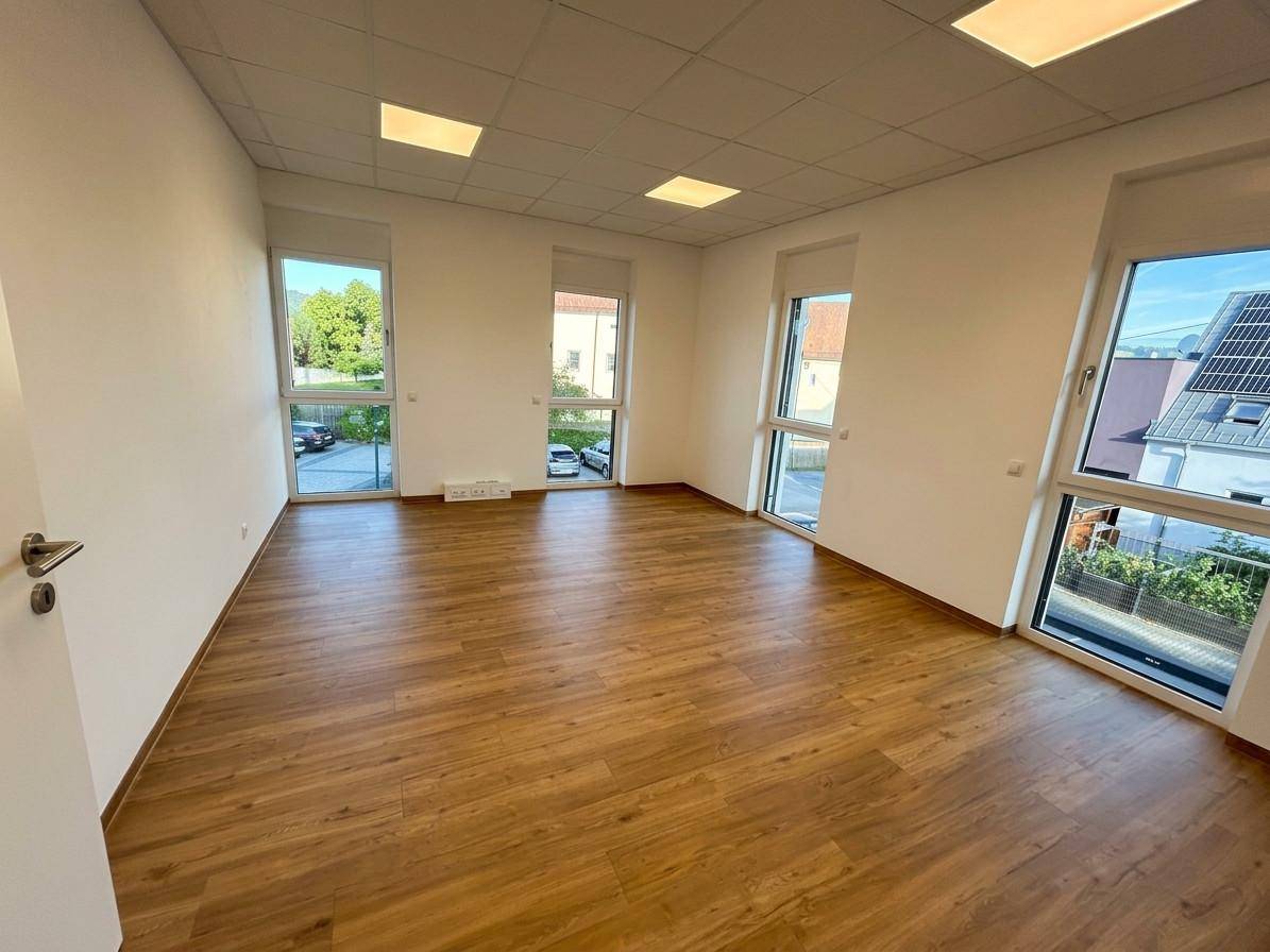Geräumiger Büroraum mit vielen großen Fenstern, Laminatboden und moderner Deckenbeleuchtung.