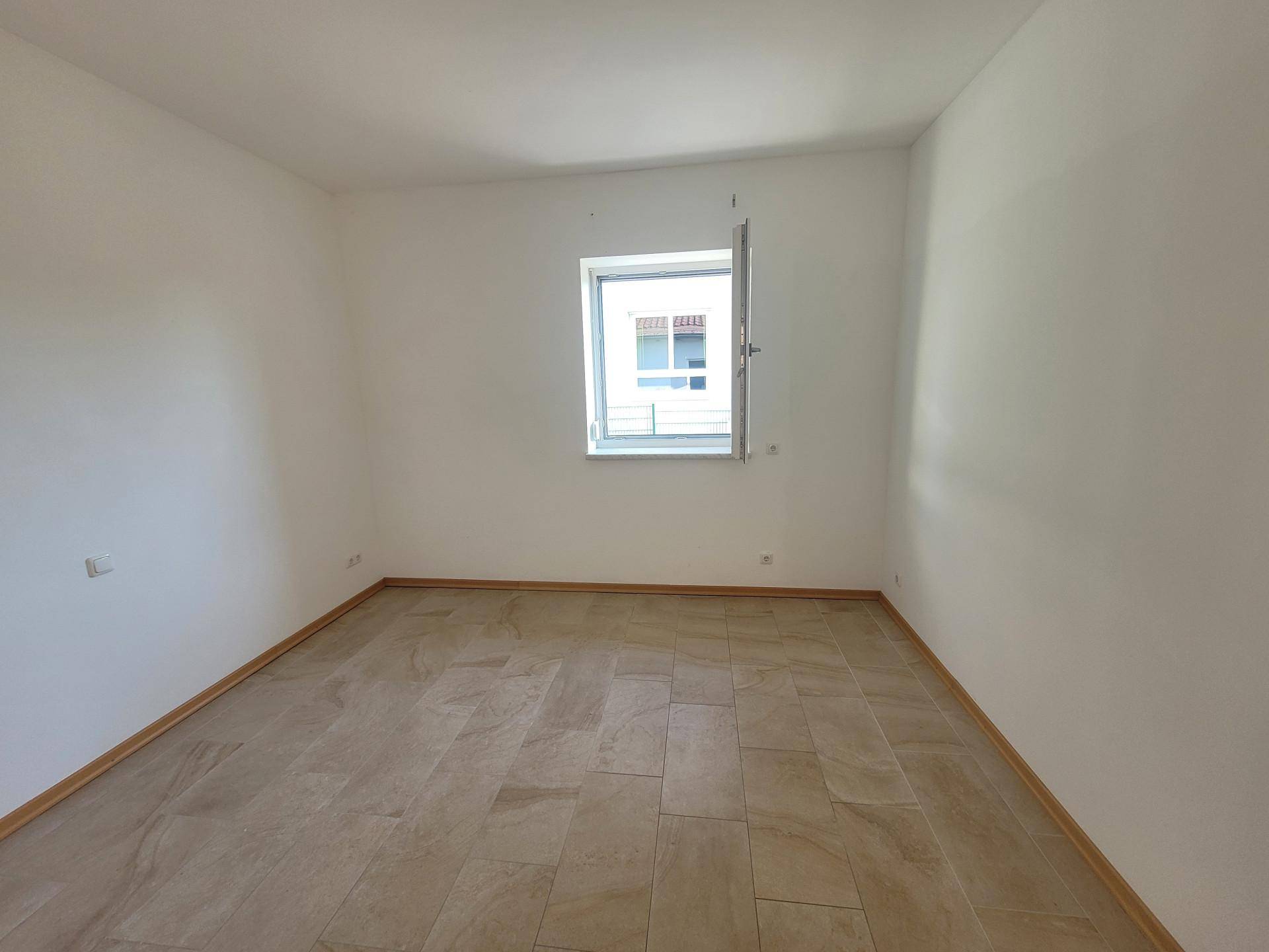 Leeres Zimmer mit Fliesenboden und einem Fenster, bereit zur individuellen Gestaltung.