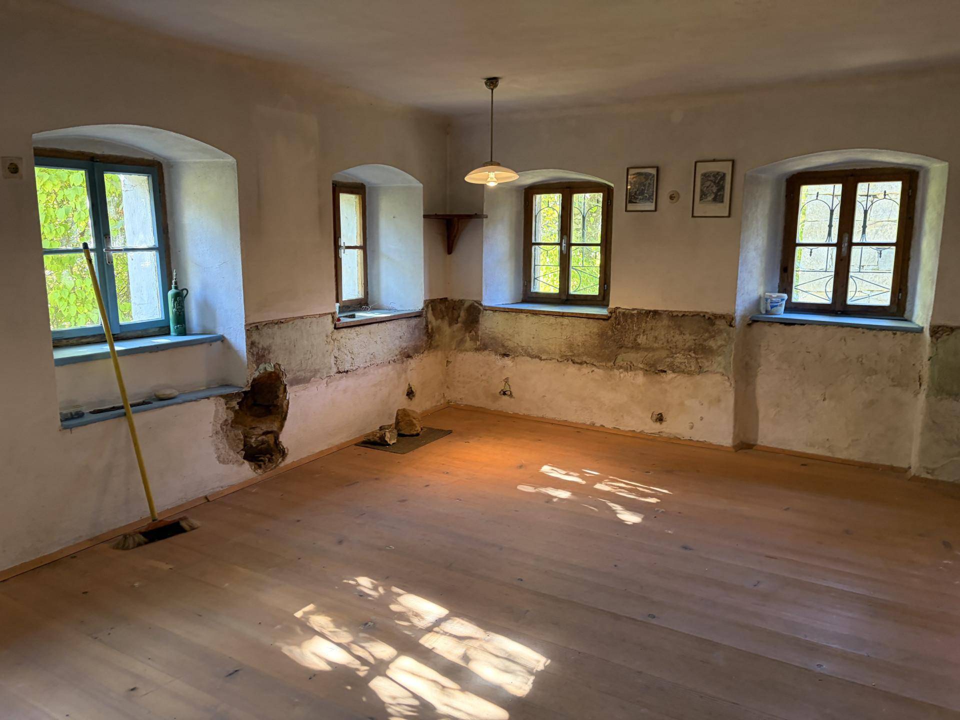 Geräumiger Wohnraum mit Holzdielenboden und mehreren Fenstern, die viel Tageslicht hereinlassen.