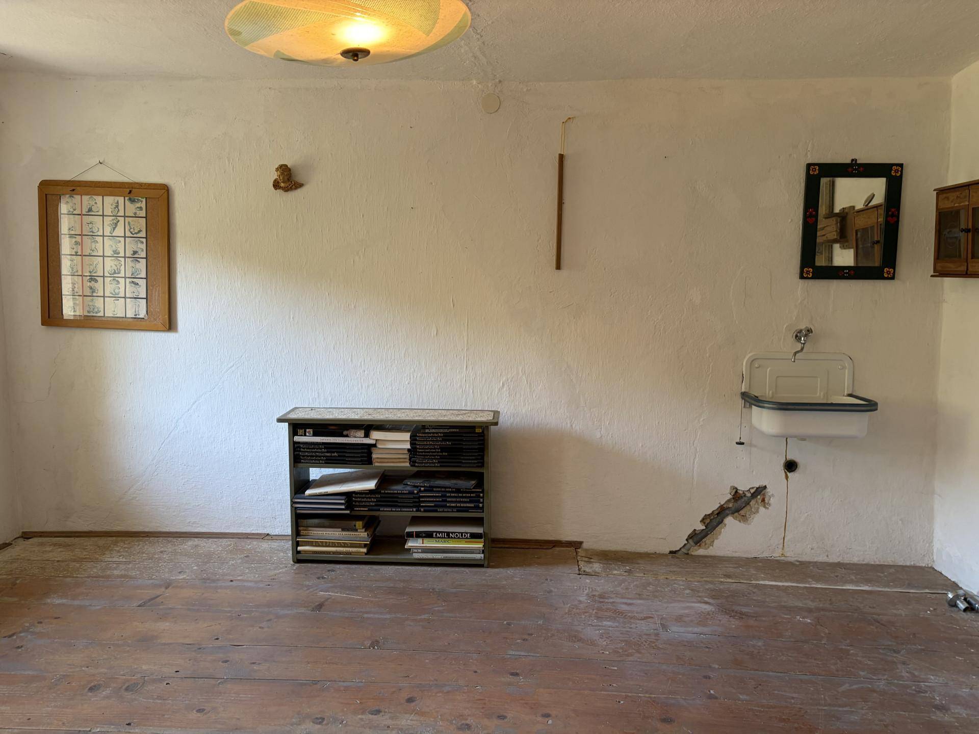 Einfacher Raum mit Holzdielenboden, einem Waschbecken und einem Regal an der Wand.