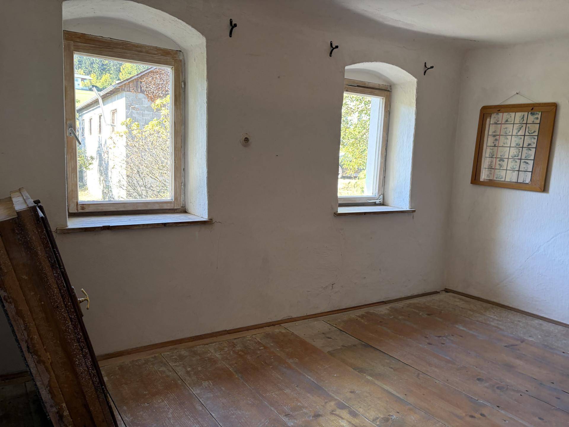 Leeres Zimmer mit Holzdielenboden und zwei Fenstern, die einen Blick nach draußen bieten.