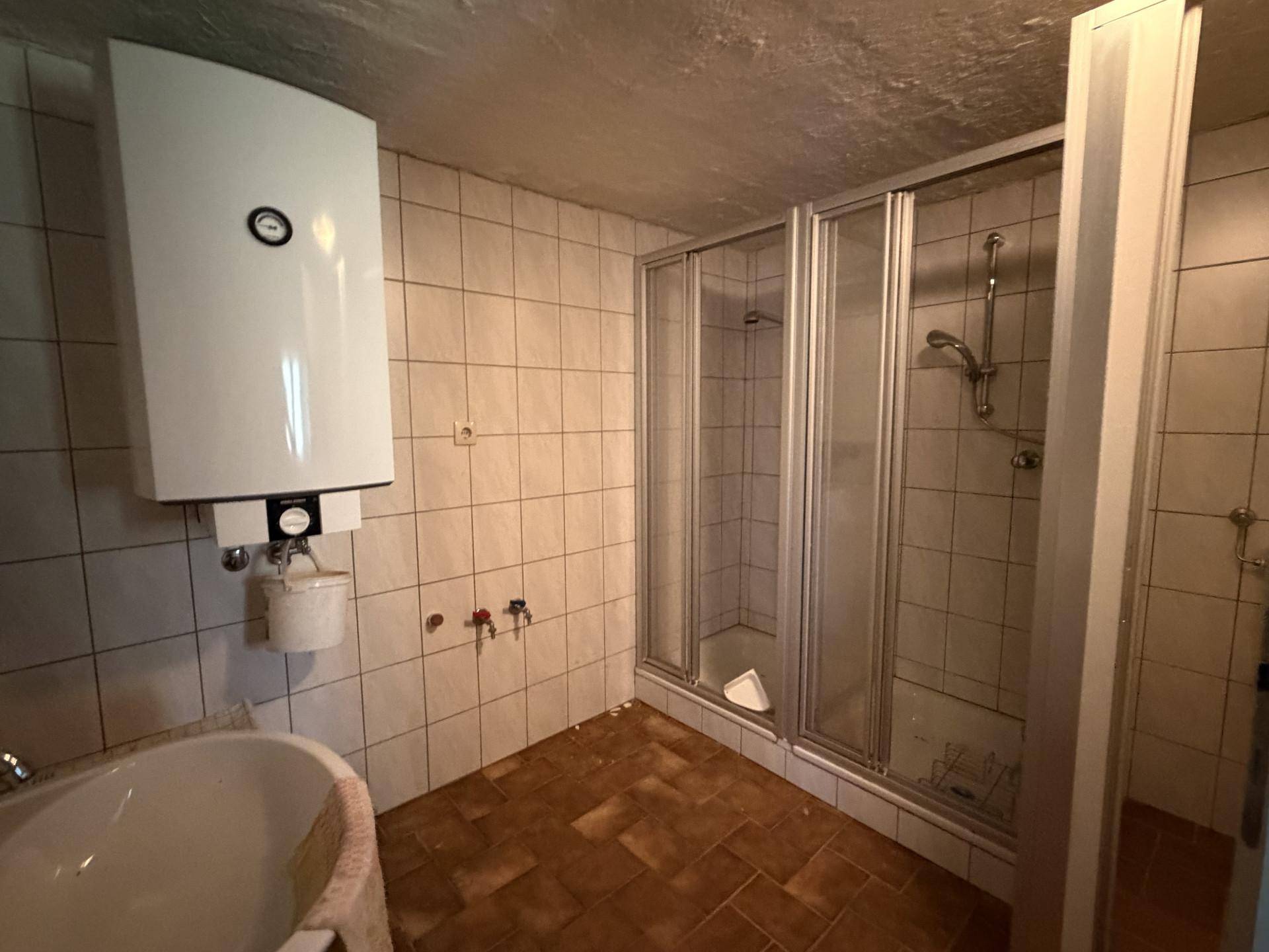 Badezimmer mit Duschkabine, Badewanne und Wandboiler, in renovierungsbedürftigem Zustand.