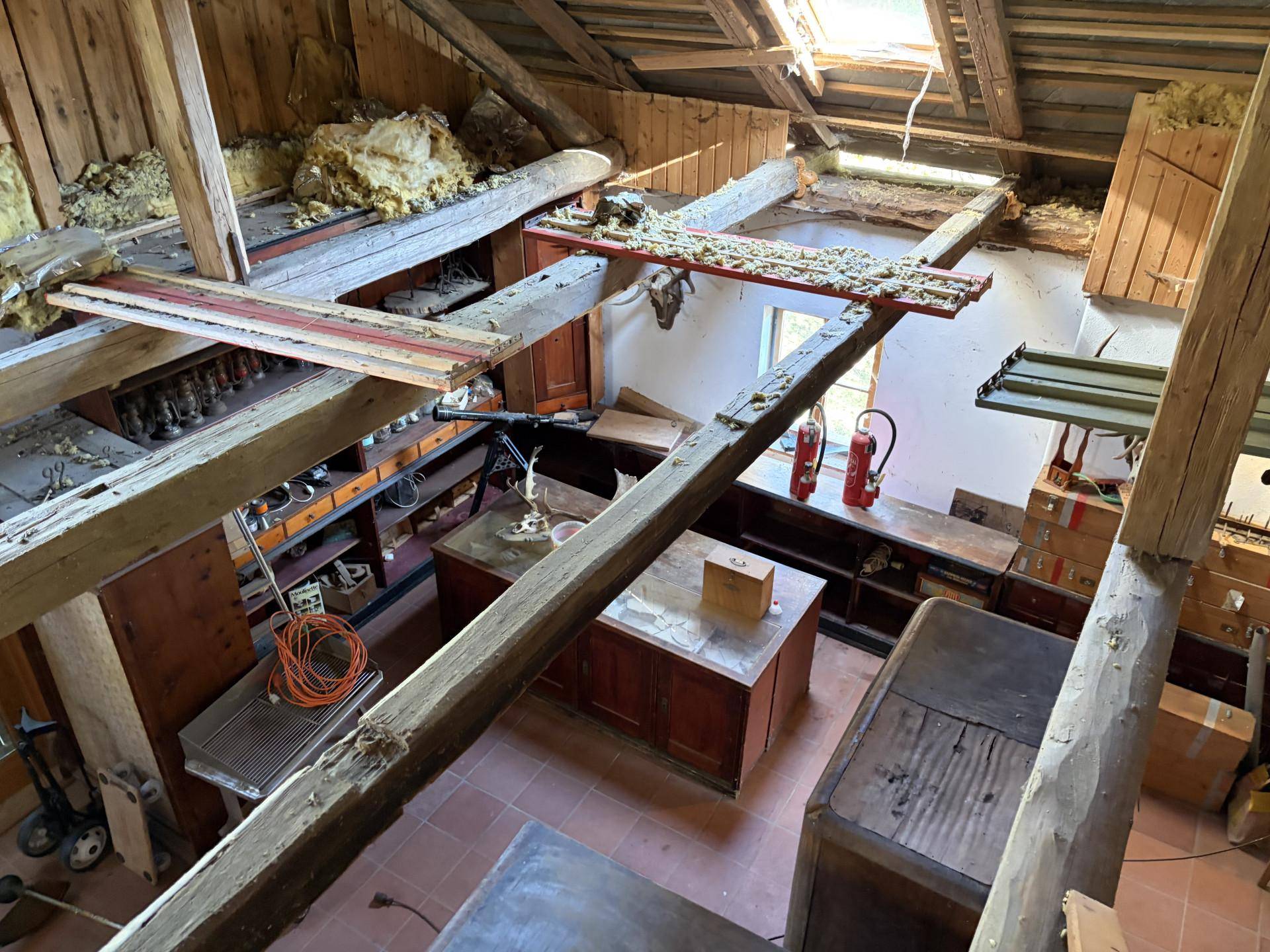 Großer Raum mit Holzbalken und alten Möbeln, möglicherweise ein ehemaliger Werkstattbereich.