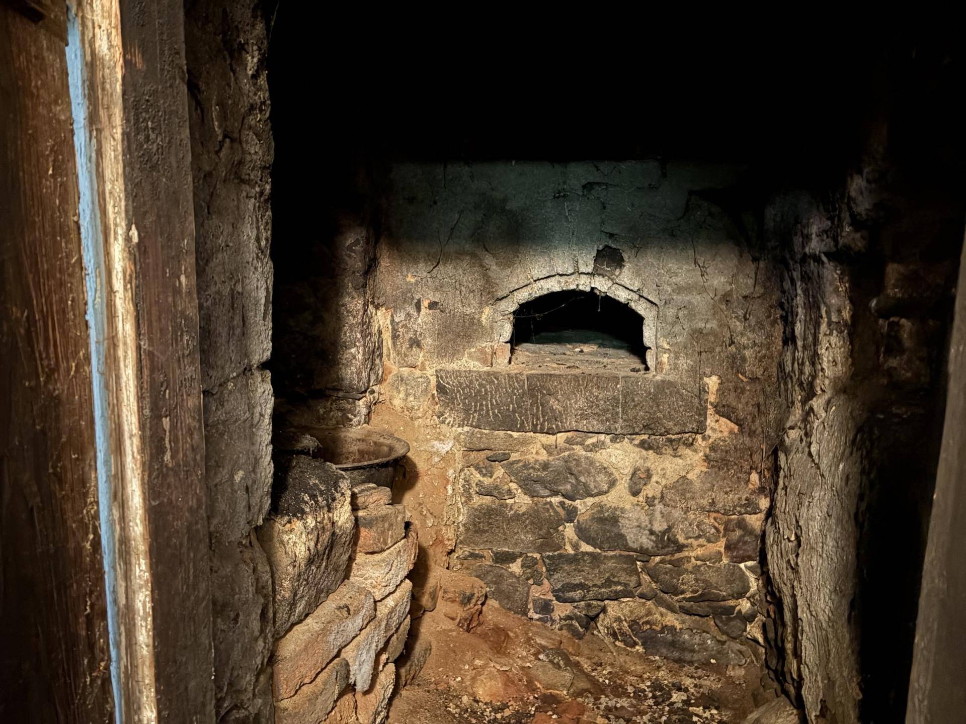 Alter, gemauerter Ofen oder Kamin in einem dunklen, rustikalen Raum mit Steinwänden.