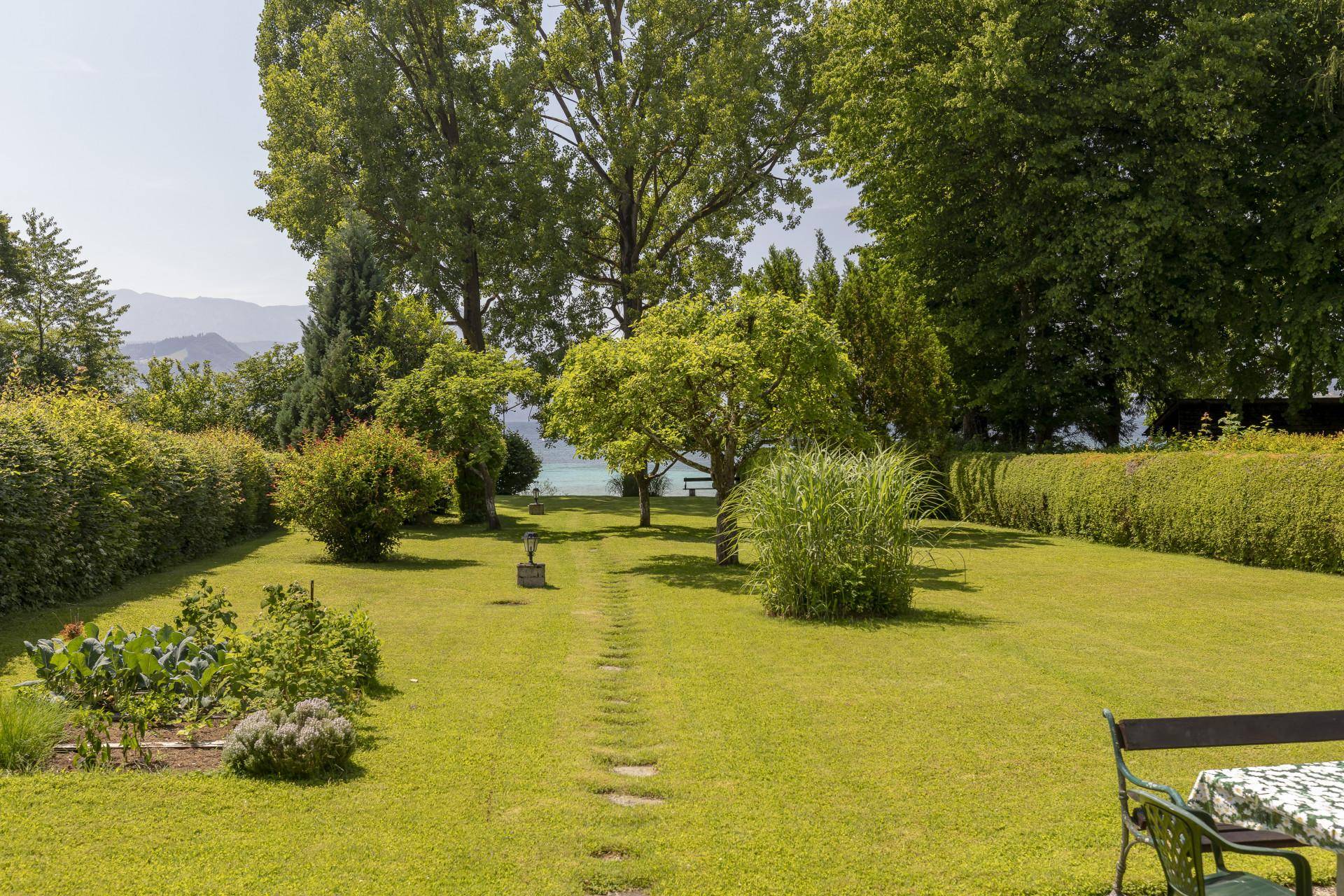 Gepflegter Garten mit Rasenfläche, Bäumen und Hecken, der einen Blick auf den See freigibt.