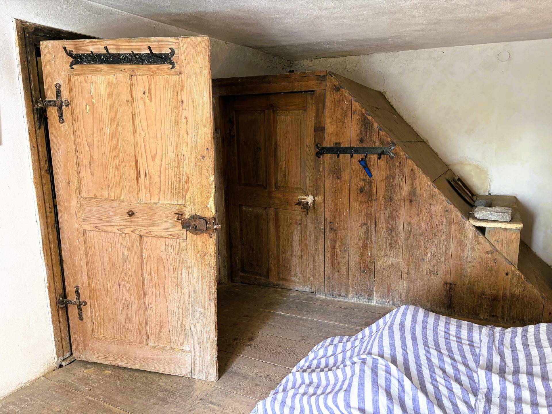 Schlafzimmer mit Holzboden und schrägen Wänden, rustikalen Holztüren und gestreifter Bettwäsche.