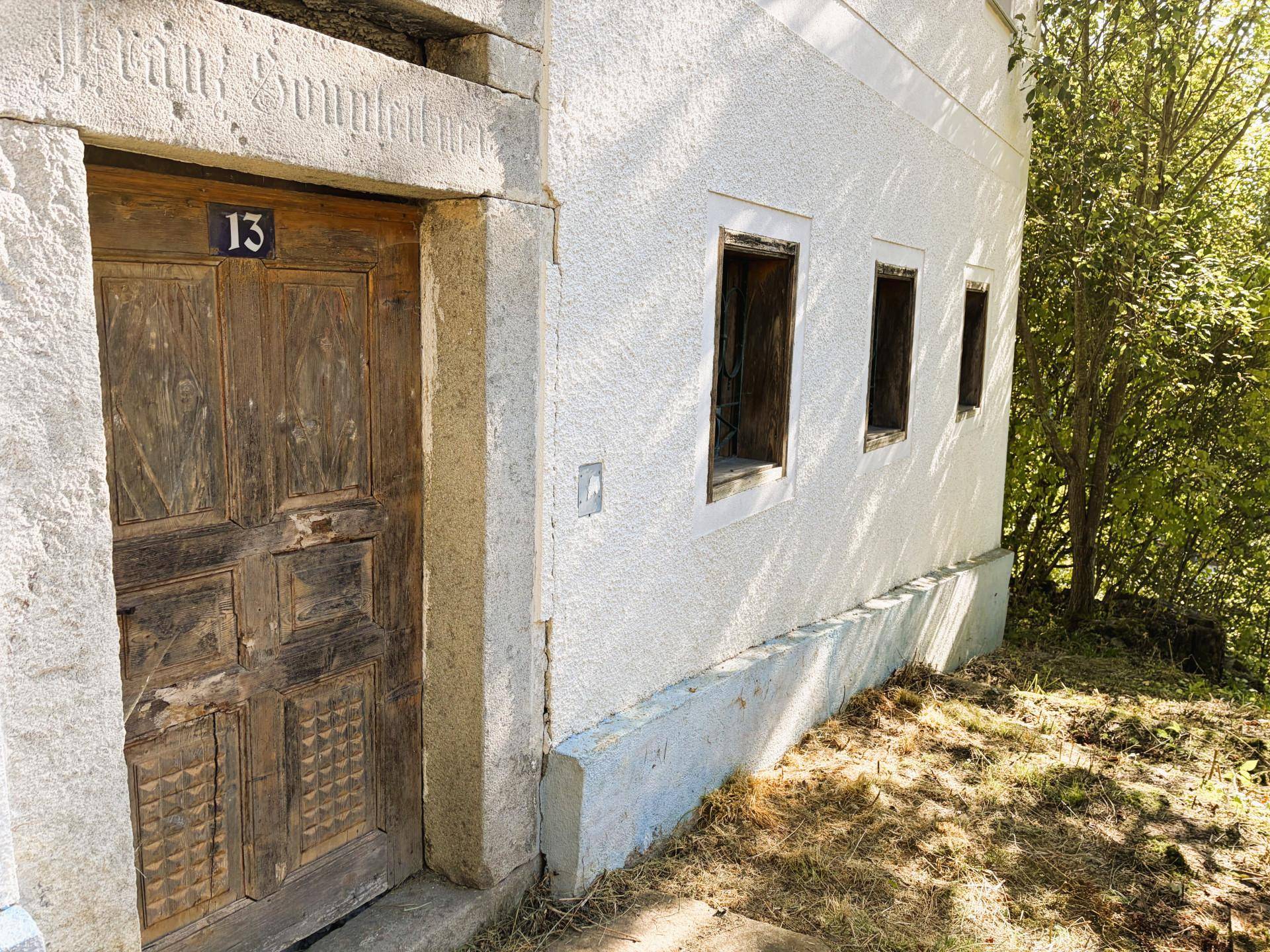 Rustikale Holztür mit der Hausnummer 13 und weißer Putzfassade eines alten Gebäudes.
