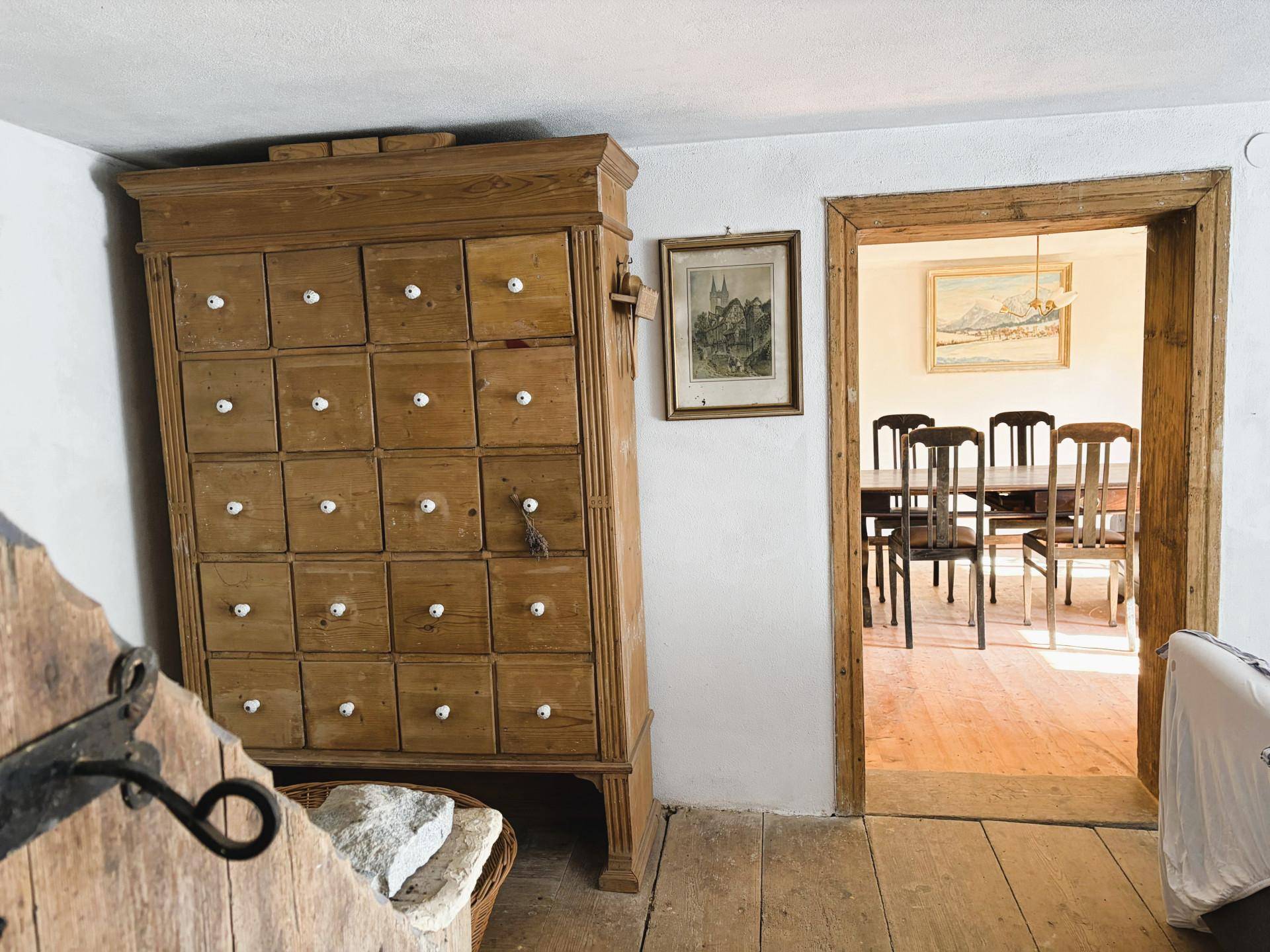 Wohnbereich mit antiker Kommode, Holzboden und Blick in einen angrenzenden Essbereich.