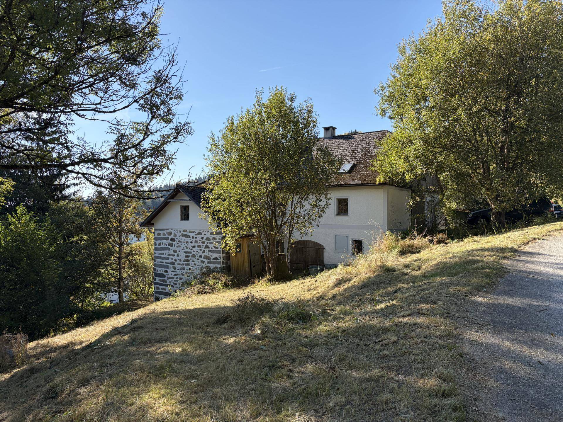 Historisches Landhaus umgeben von Bäumen und einem Feldweg unter klarem Himmel.