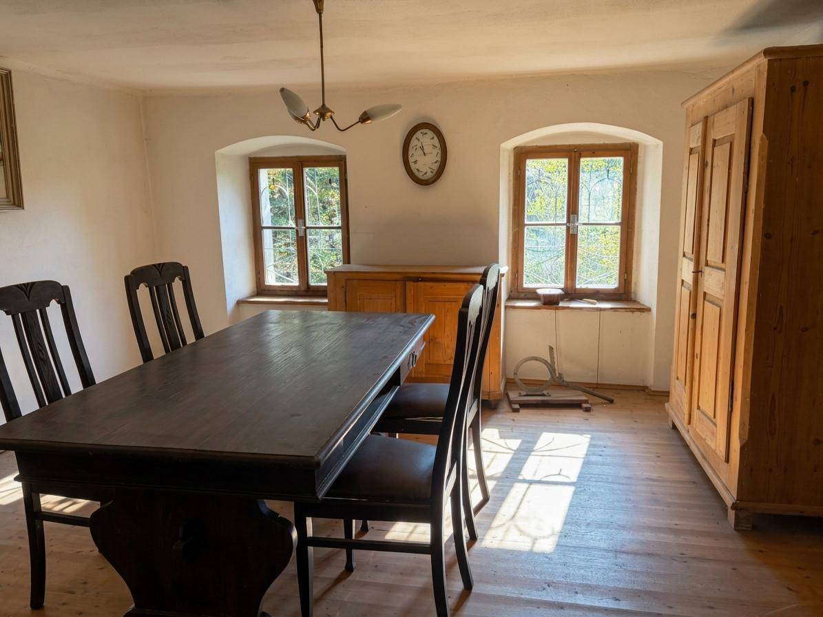 Esszimmer mit dunklem Holztisch, passenden Stühlen und zwei Fenstern mit Blick ins Grüne.