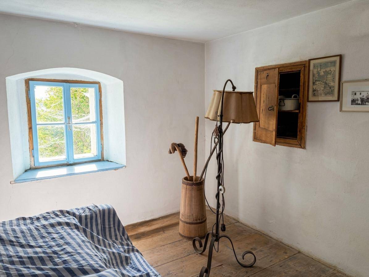 Helles Schlafzimmer mit Holzboden, einem Fenster mit blauen Rahmen und einer Stehlampe.