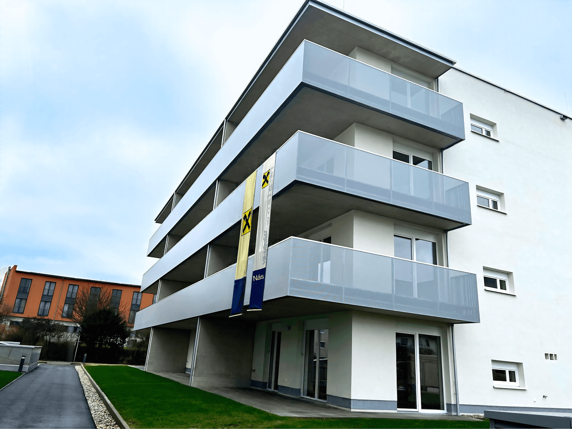 Moderne Gebäudefassade mit großen Balkonen und Werbebannern an einem bewölkten Tag.