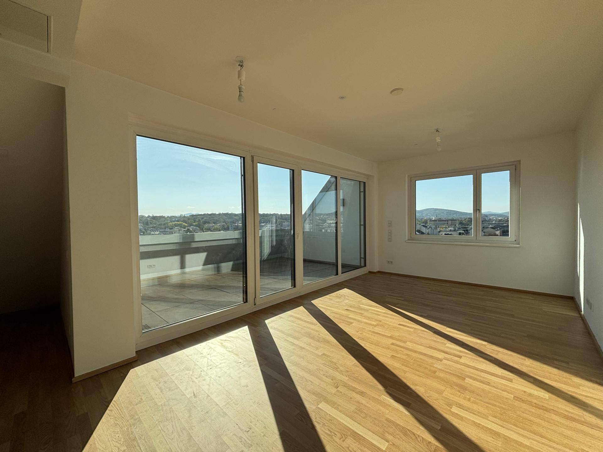 Geräumiges Wohnzimmer mit Holzboden, großen Fenstern und Zugang zur Terrasse, bietet einen weiten Stadtblick.