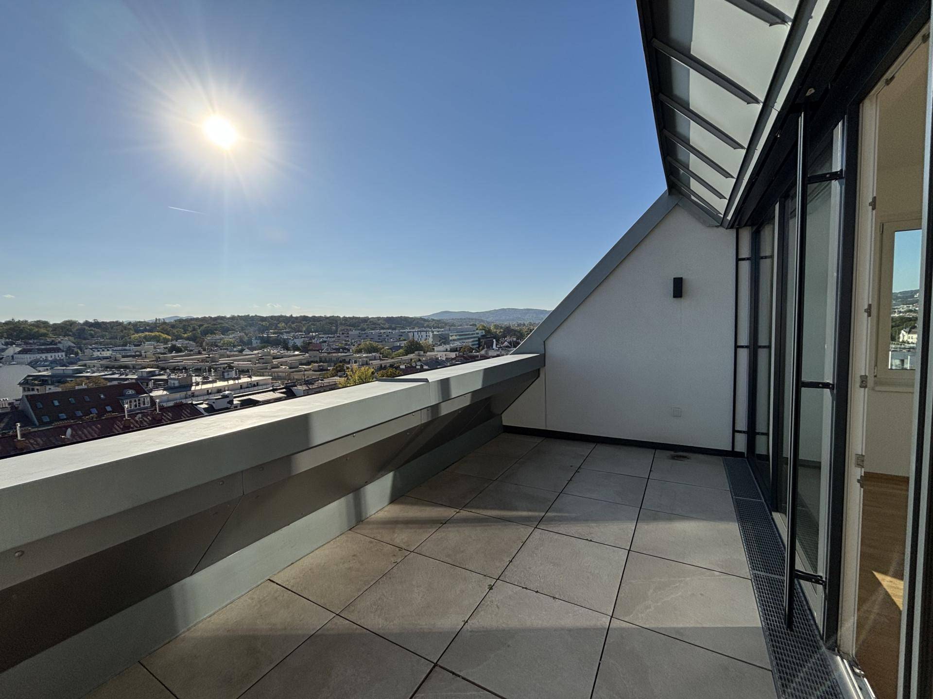 Große Dachterrasse mit Fliesenboden und weitem Blick über die Stadt unter strahlendem Sonnenschein.