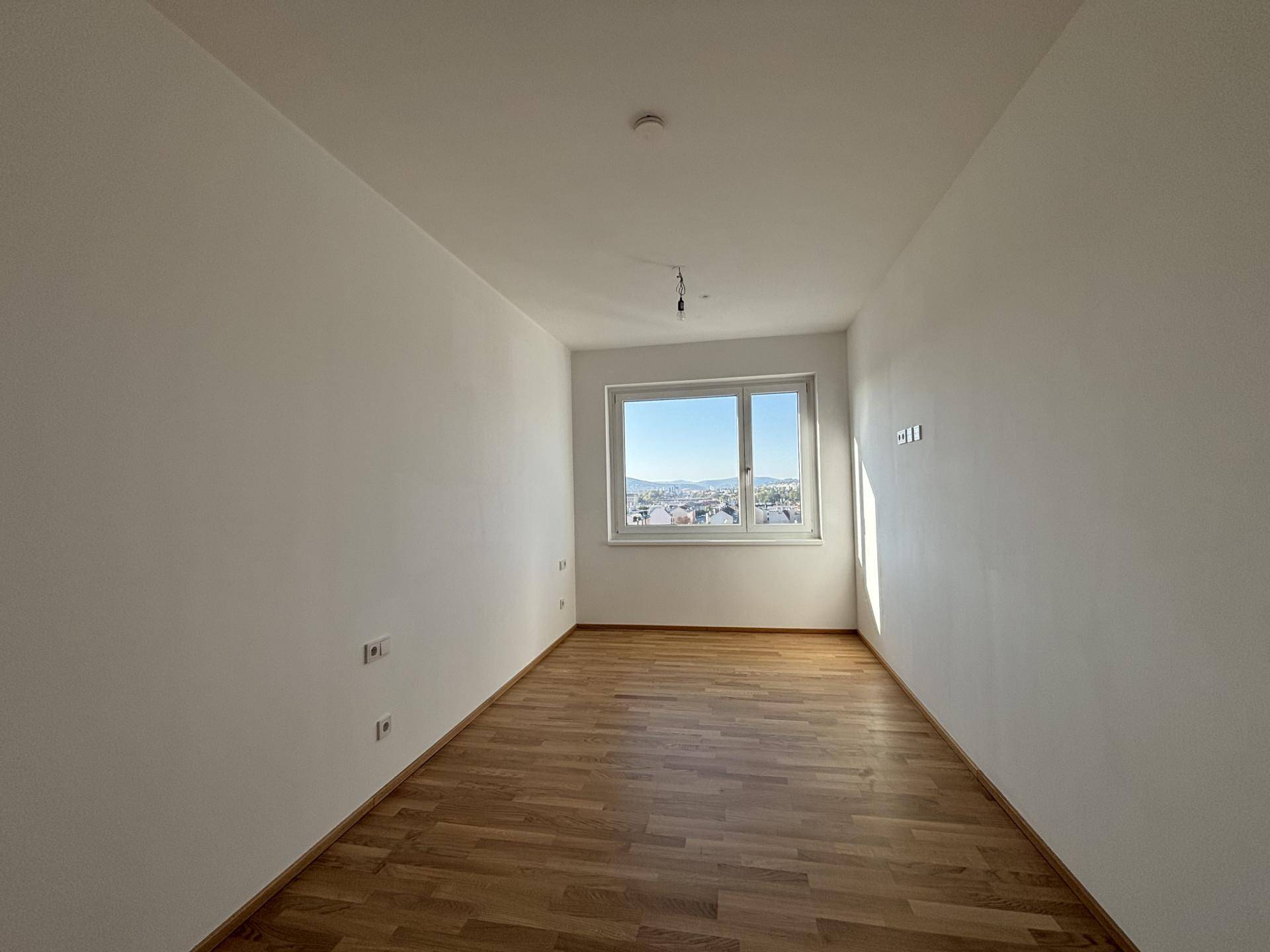 Geräumiges, helles Zimmer mit Parkettboden und Fenster, ideal als Schlafzimmer oder Arbeitsbereich nutzbar.