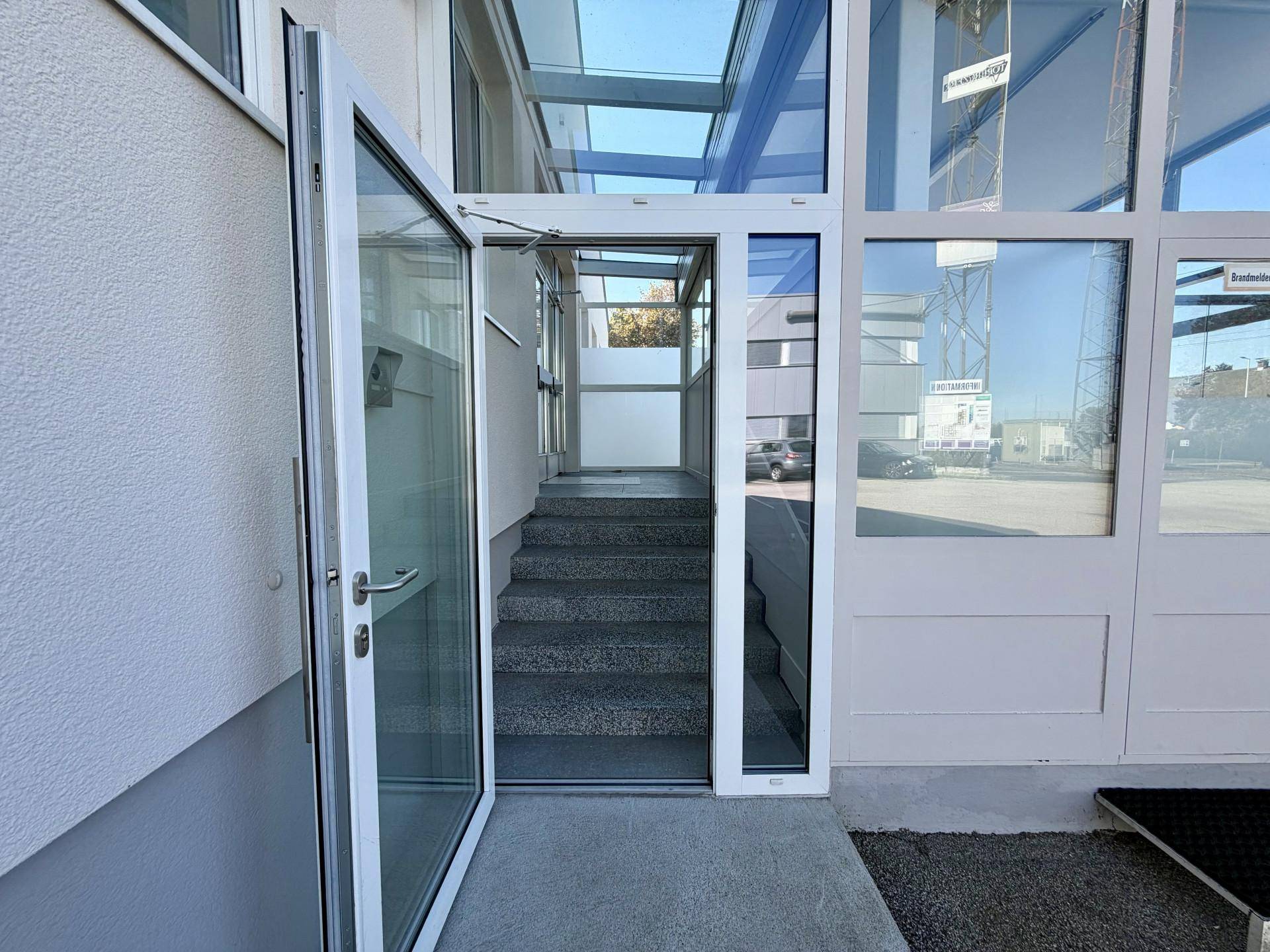 Heller Eingangsbereich mit Glastür und Treppe, die in die oberen Etagen führt.