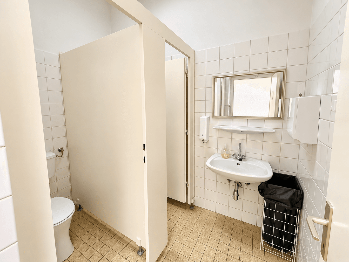 Sauberer öffentlicher Toilettenraum mit mehreren Kabinen, Waschbecken und Fliesenboden.