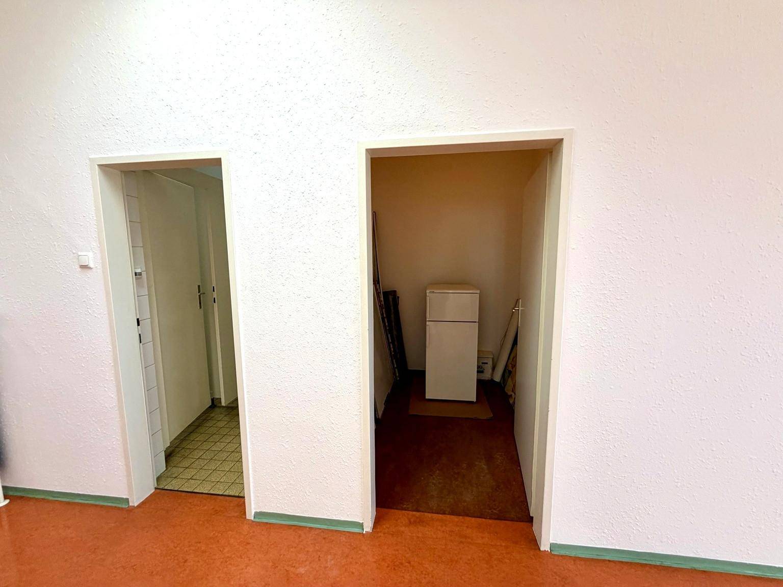 Kleiner Abstellraum mit Kühlschrank und Zugang zu einem weiteren Raum, praktisch und funktional.