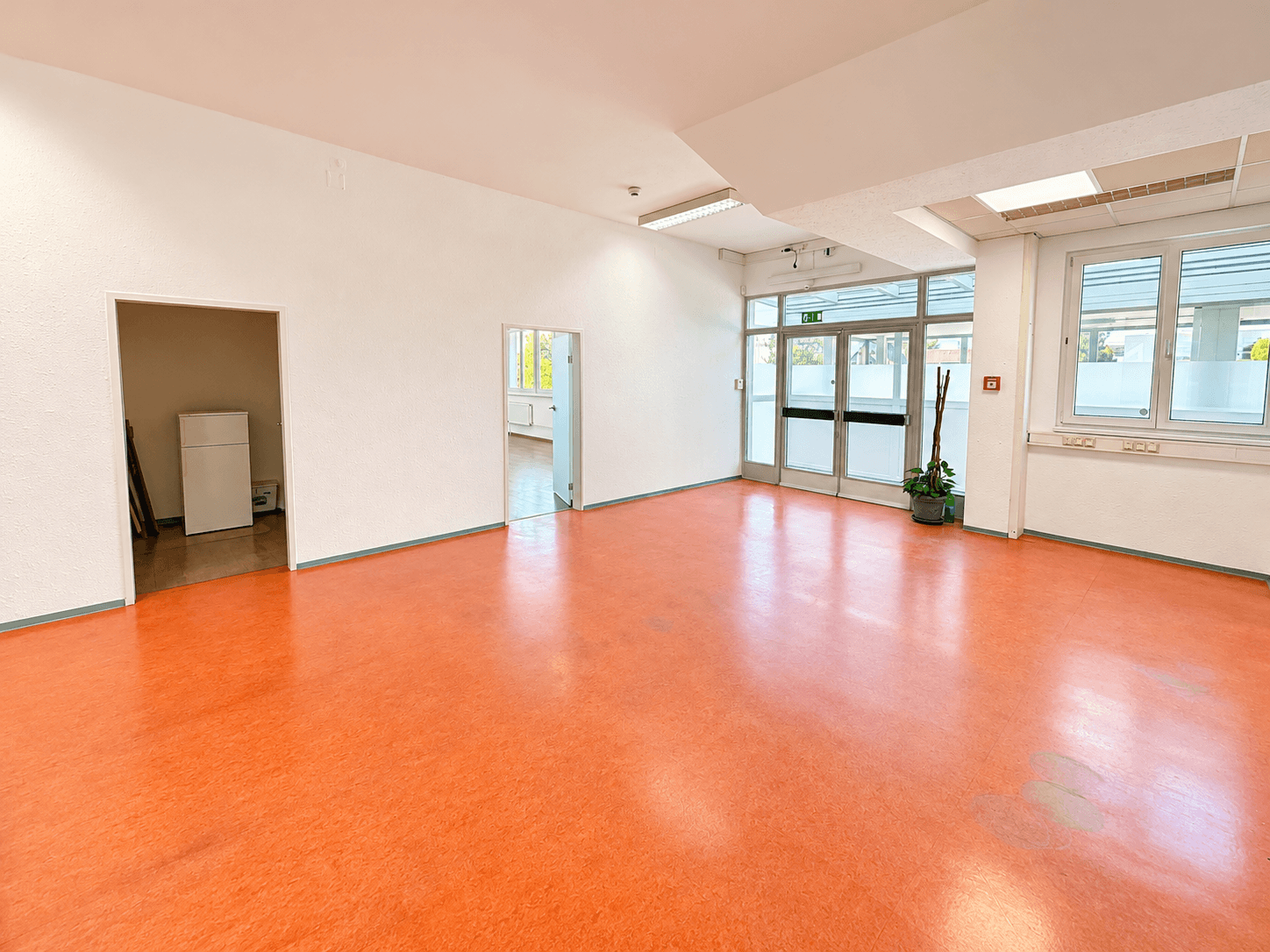 Geräumiger, leerer Raum mit leuchtend orangefarbenem Boden und großen Fenstern, bereit zur Einrichtung.
