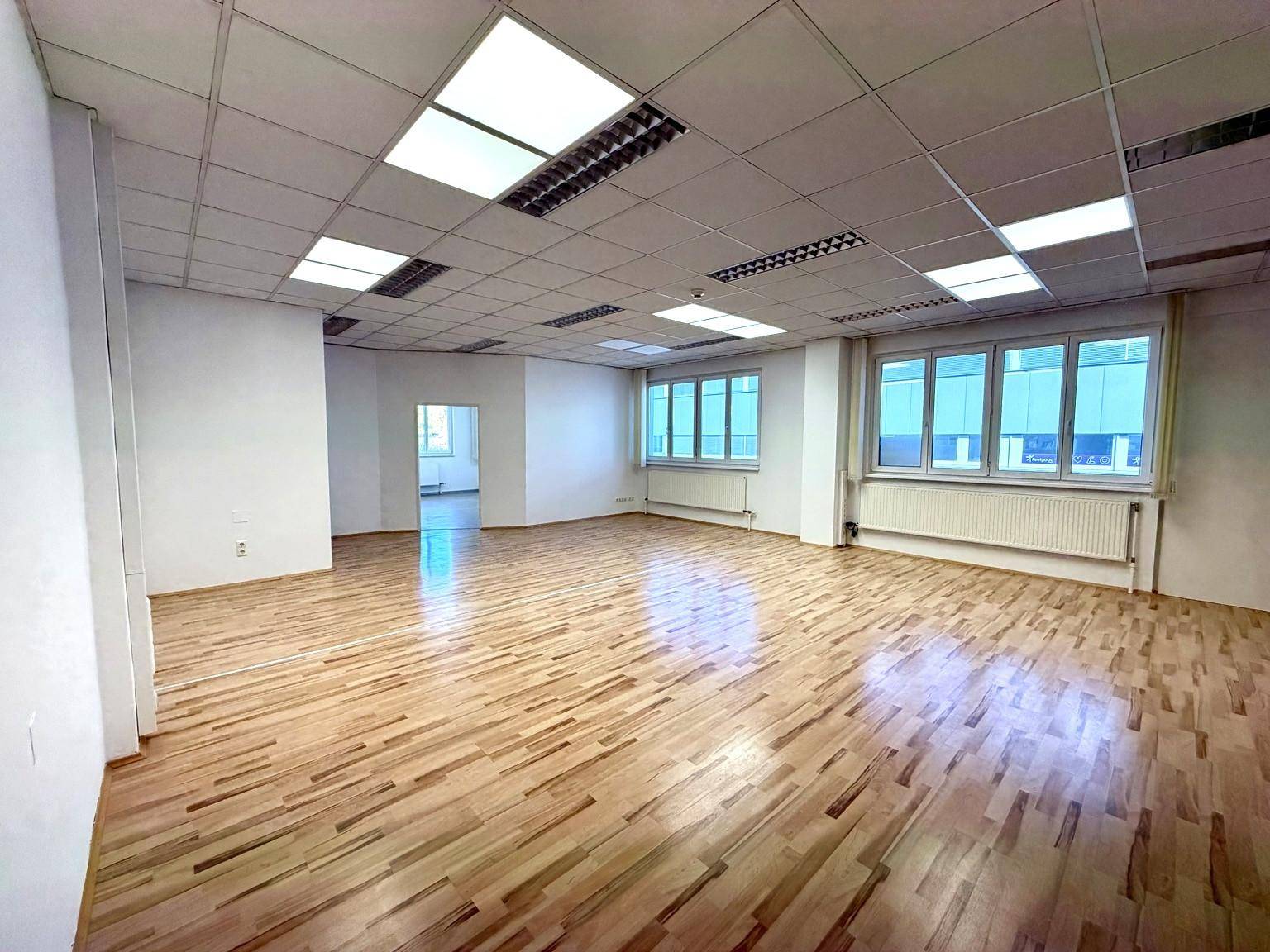 Heller Büroraum mit Holzboden und großen Fenstern, bietet viel Tageslicht für angenehmes Arbeiten.