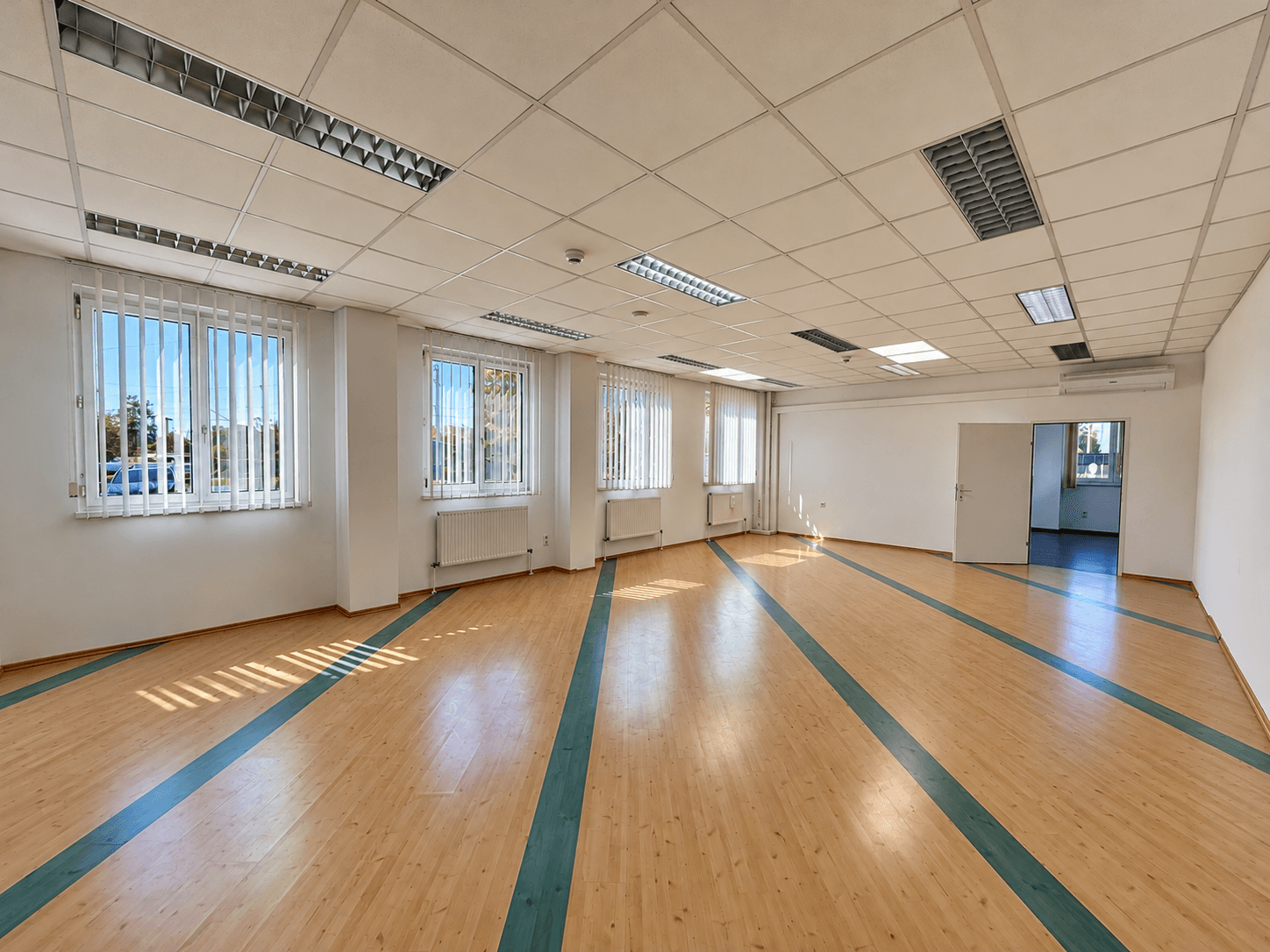 Großer, heller Büroraum mit Holzboden und blauen Akzentstreifen, ideal für kreative Arbeitsbereiche.