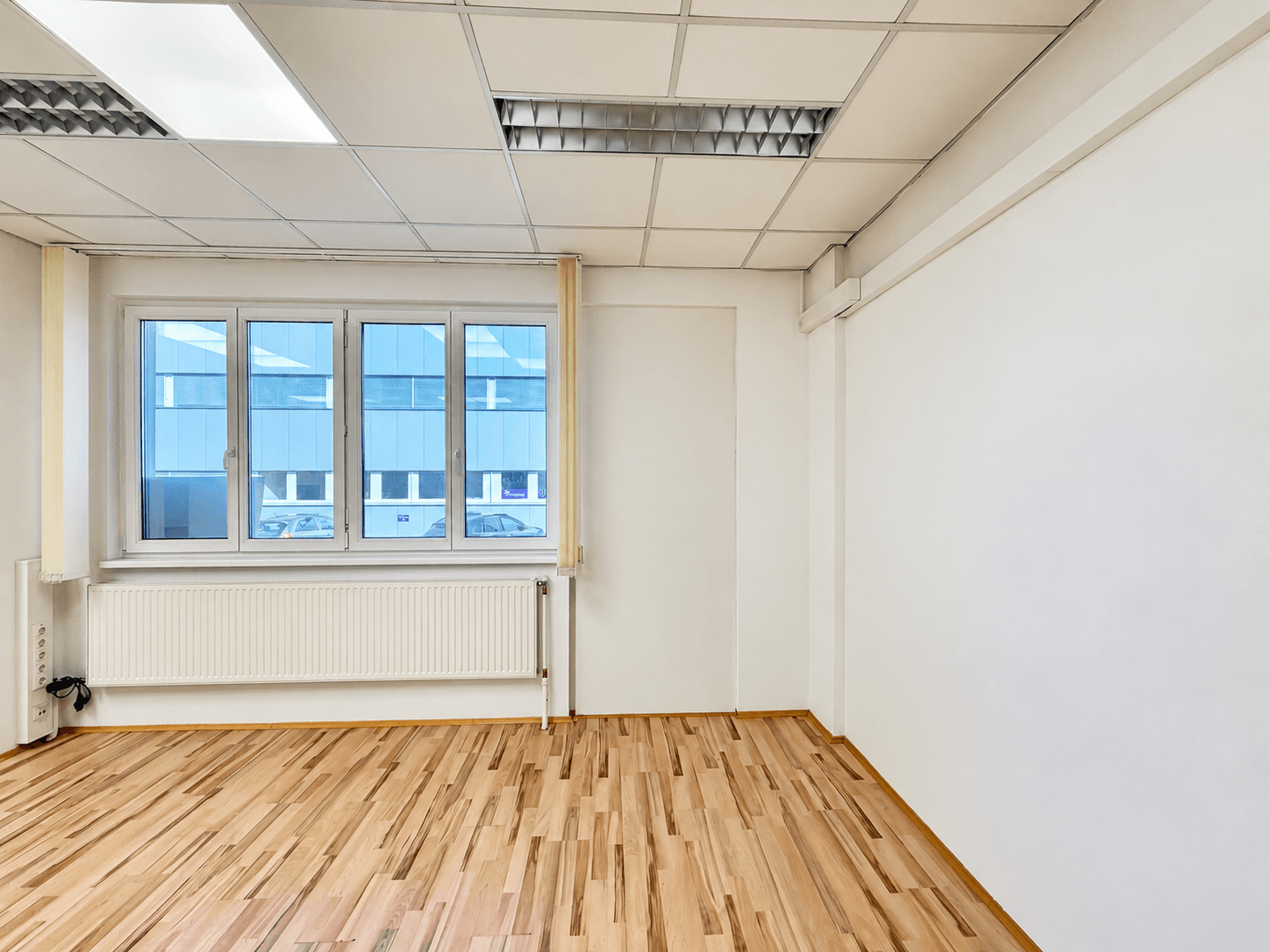 Heller Büroraum mit Holzboden und großen Fenstern, bietet viel Tageslicht für produktives Arbeiten.