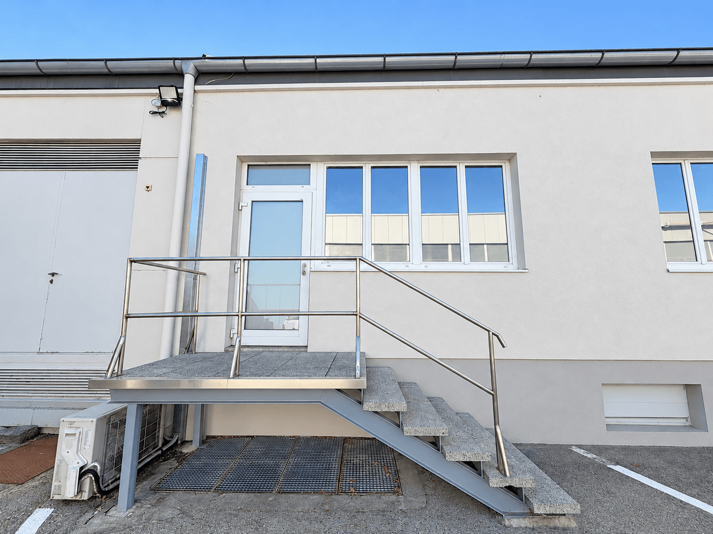Seitlicher Eingang eines Gebäudes mit Metalltreppe und Geländer, führt zu einer Tür.