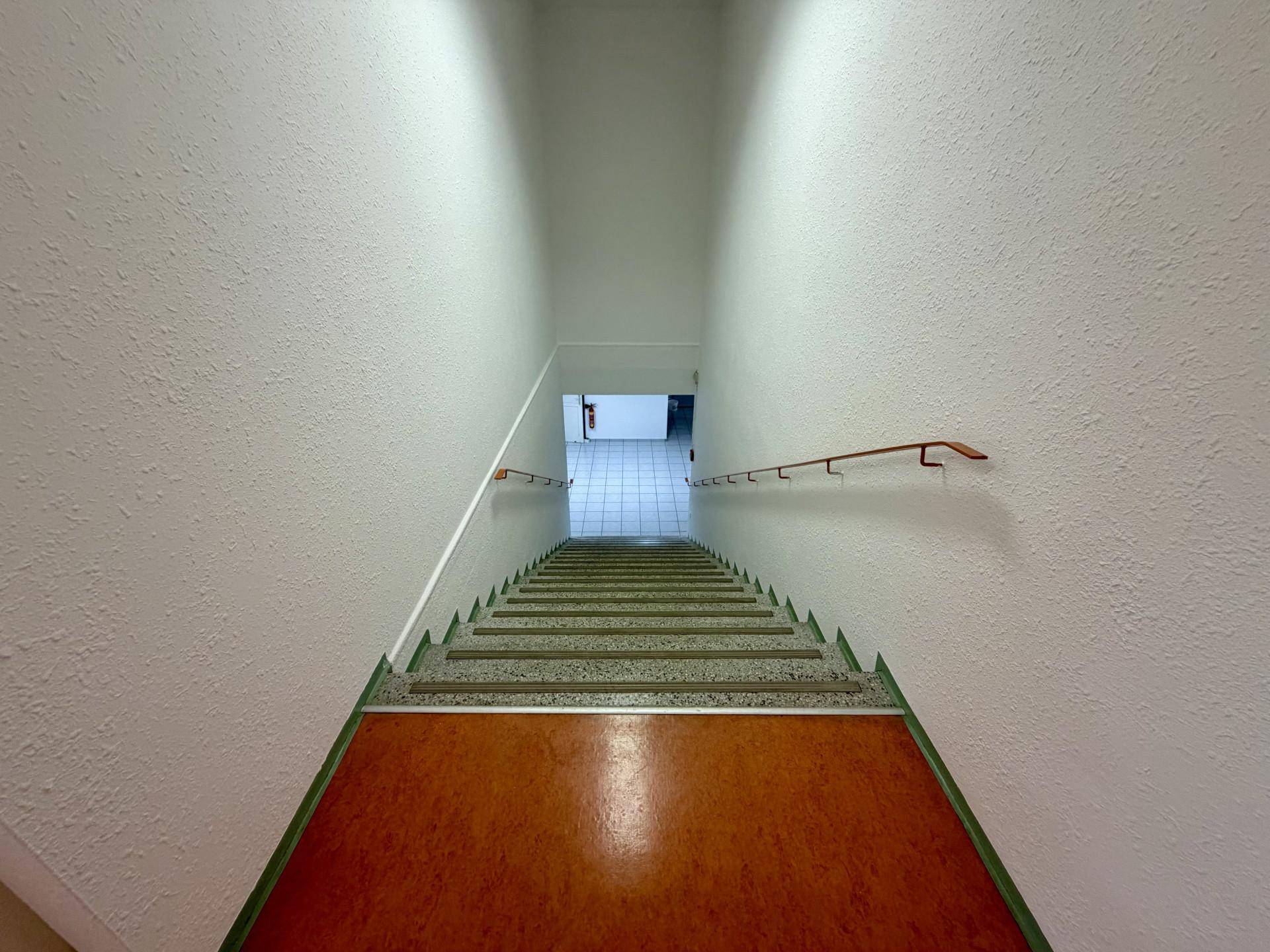 Langer Treppenaufgang mit Handläufen und Terrazzostufen, führt zu weiteren Etagen.