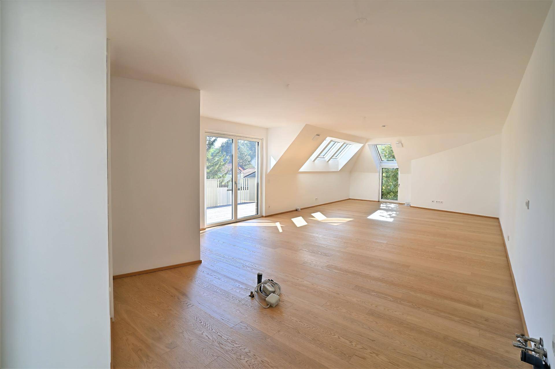 Geräumiger, leerer Wohn-Essbereich mit Holzboden und Zugang zum Balkon.