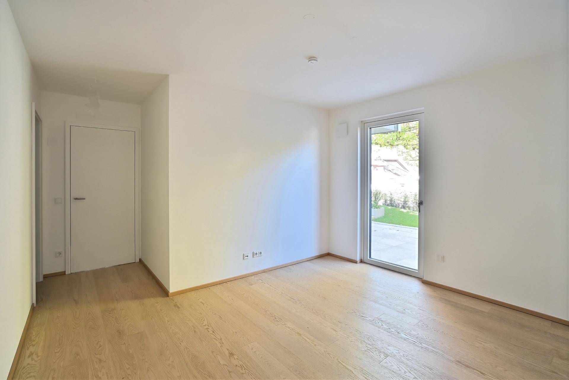 Unmöbliertes Schlafzimmer mit hellem Holzboden und Zugang zum Garten, bietet viel Gestaltungspotenzial.