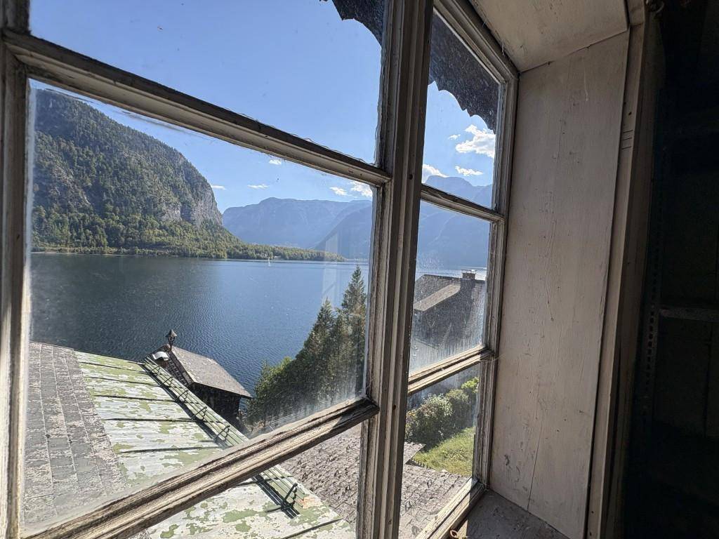 Blick durch ein altes Fenster auf den See und die majestätische Berglandschaft.