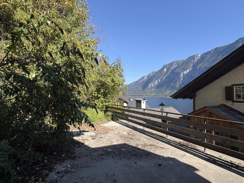 Außenweg mit Holzzaun und weitem Blick auf den See und die umliegende Berglandschaft.