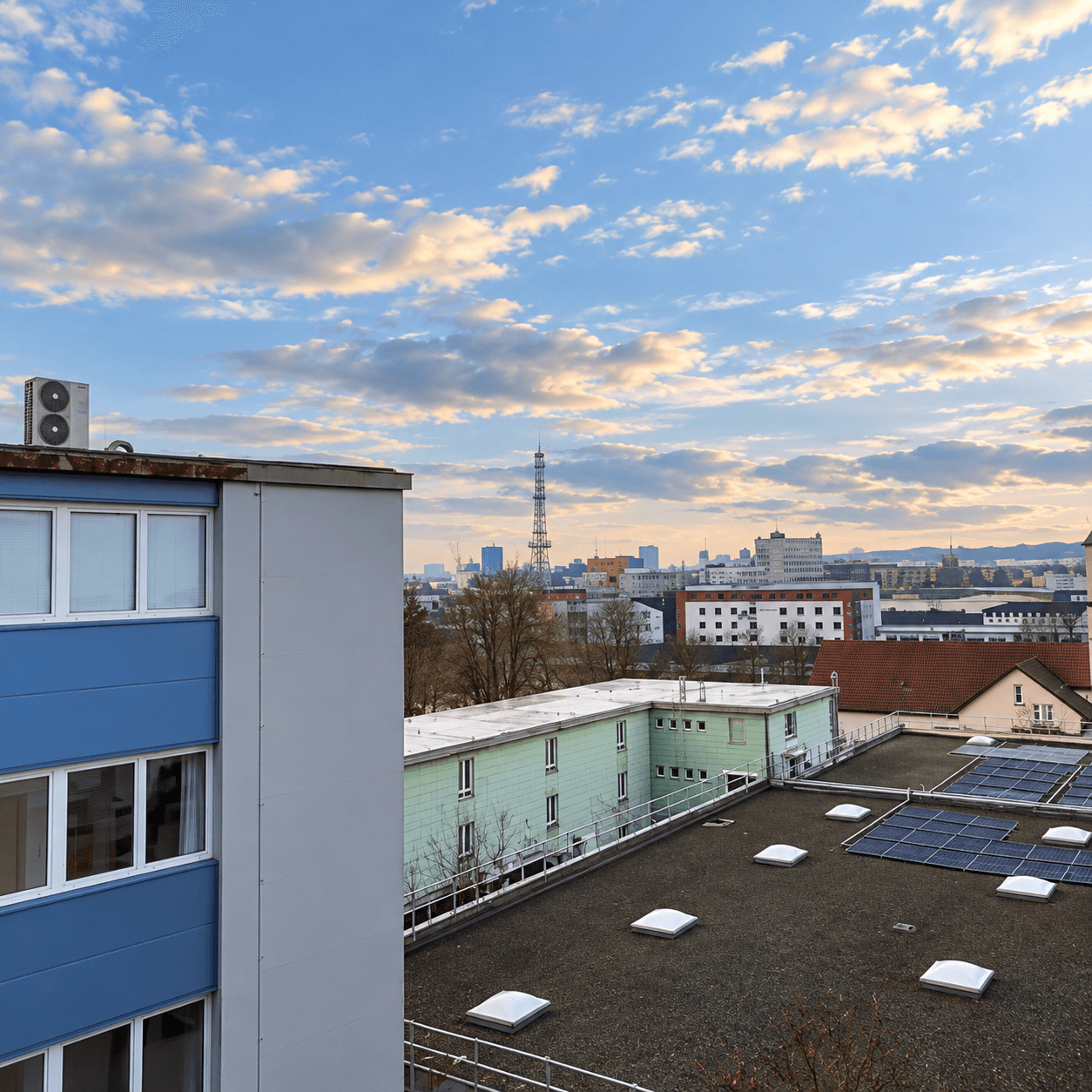 Dachlandschaft mit Solaranlagen und Blick auf die Stadt unter einem bewölkten Himmel.