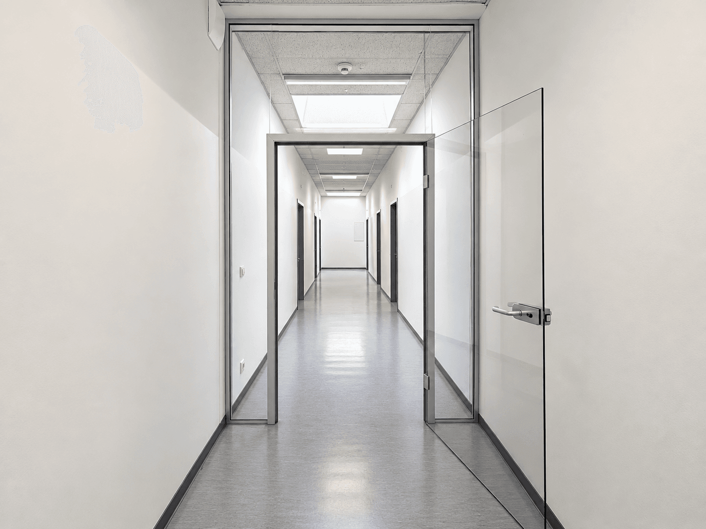 Langer, heller Flur mit Glaswänden und Türen, der zu weiteren Räumen in einem Bürogebäude führt.